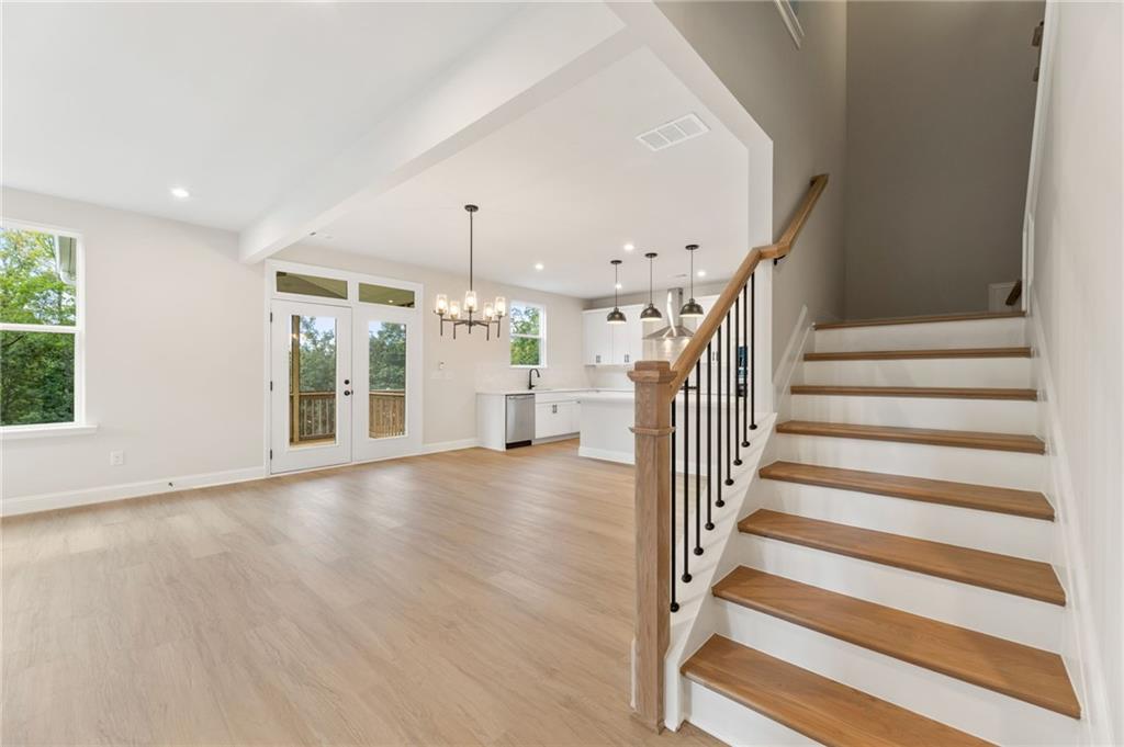 Bright open-concept kitchen-living area with white cabinets, hardwood floors, staircase, and French doors to deck in 5-bedroom Davidson Homes The Hickory B, Buford, Georgia