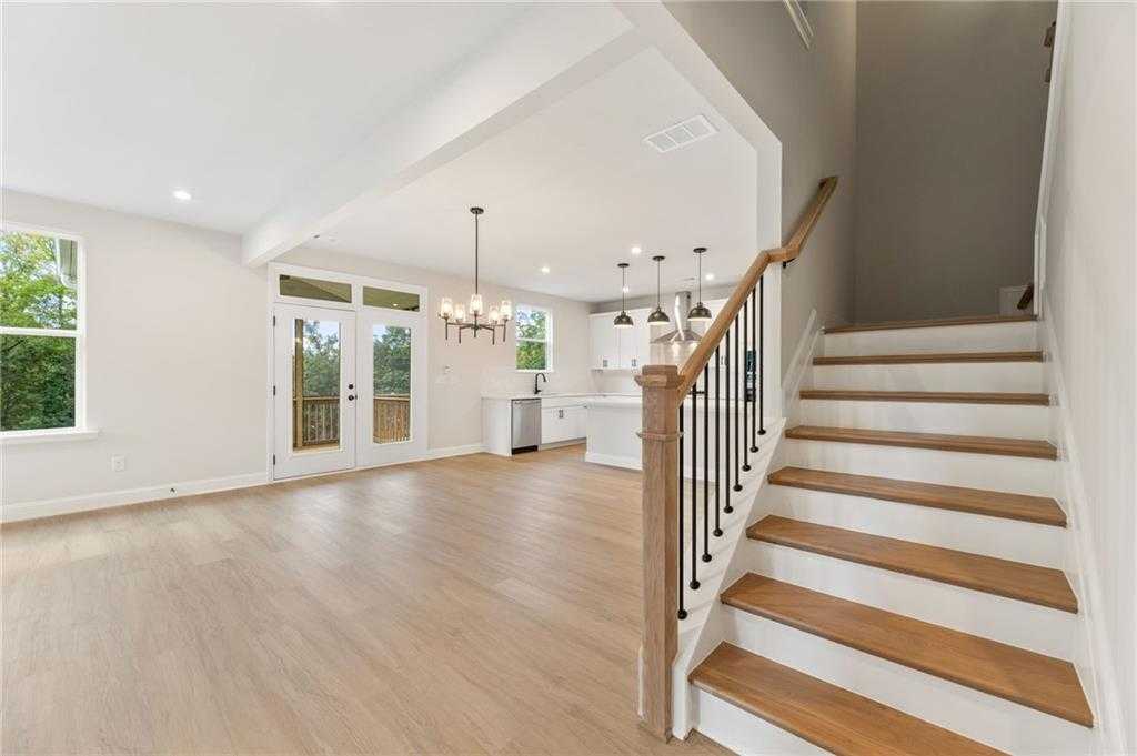 Bright open-concept kitchen-living area with white cabinets, hardwood floors, staircase, and French doors to deck in 5-bedroom Davidson Homes The Hickory B, Buford, Georgia
