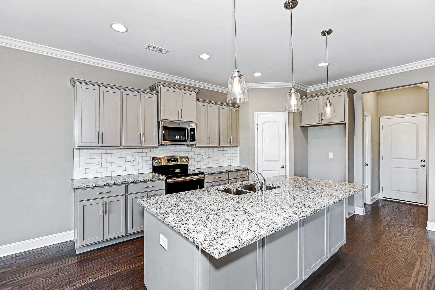Modern kitchen in The Montgomery by Davidson Homes featuring gray shaker cabinets, granite island, subway tile backsplash, and stainless appliances