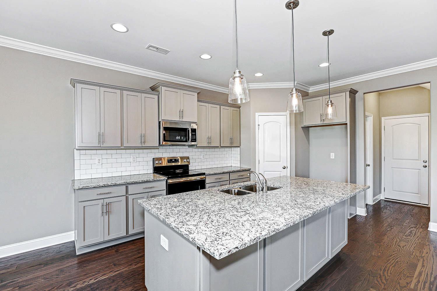 Modern kitchen in The Montgomery by Davidson Homes featuring gray shaker cabinets, granite island, subway tile backsplash, and stainless appliances
