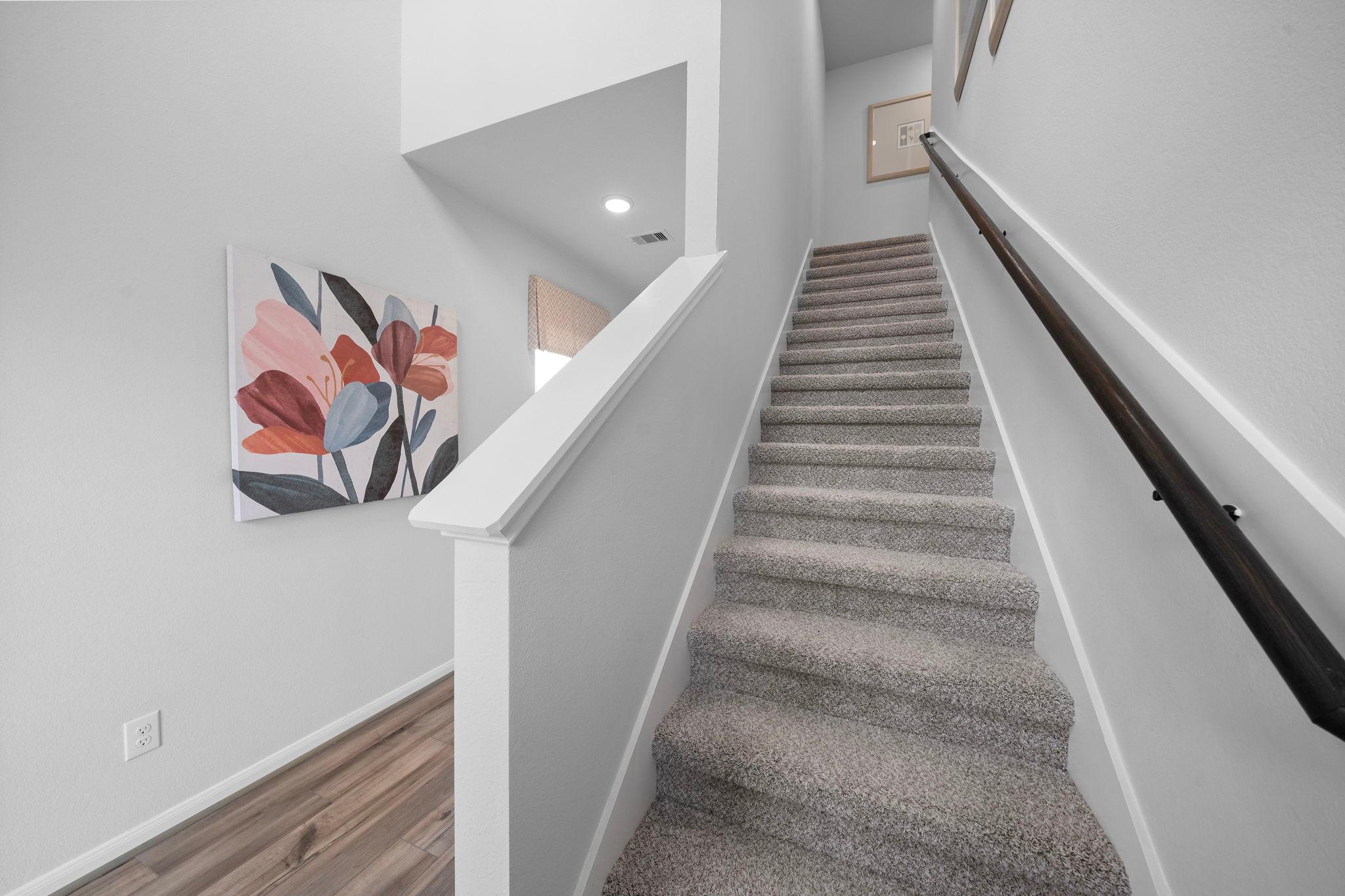 Carpeted staircase with black handrail and pink floral wall art in Hill & Dale Ranch home, Splendora Texas by Davidson Homes