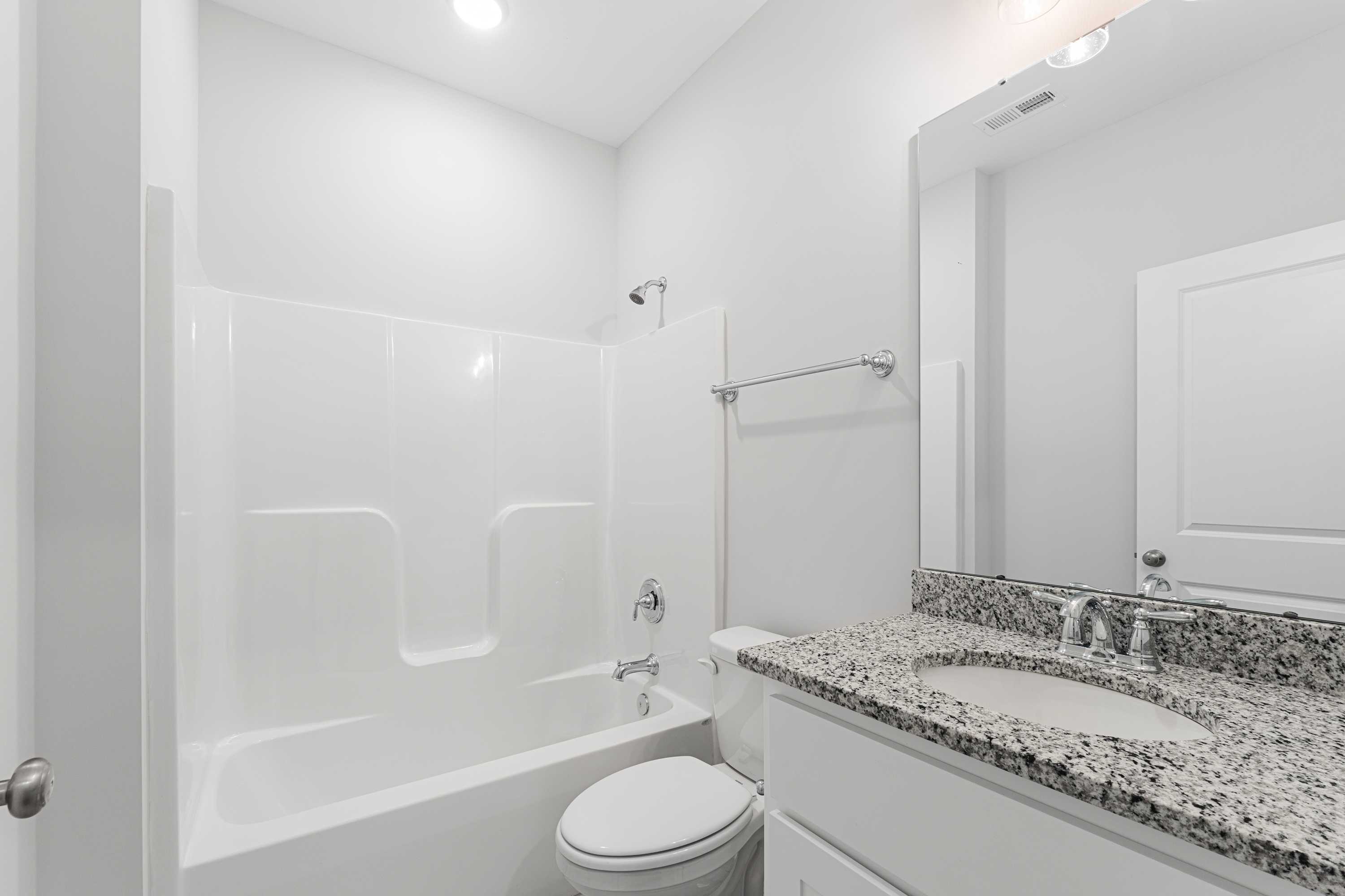 Spacious guest bathroom in The Copeland B featuring white tub-shower combo, granite vanity, sleek mirror, and modern fixtures