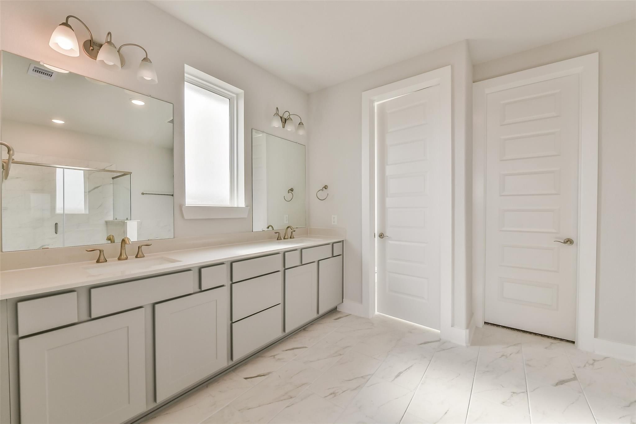 Elegant master bathroom with double vanity, brass fixtures, mirrors, and tiled floor in Davidson Homes The George A, Lago Mar, Texas