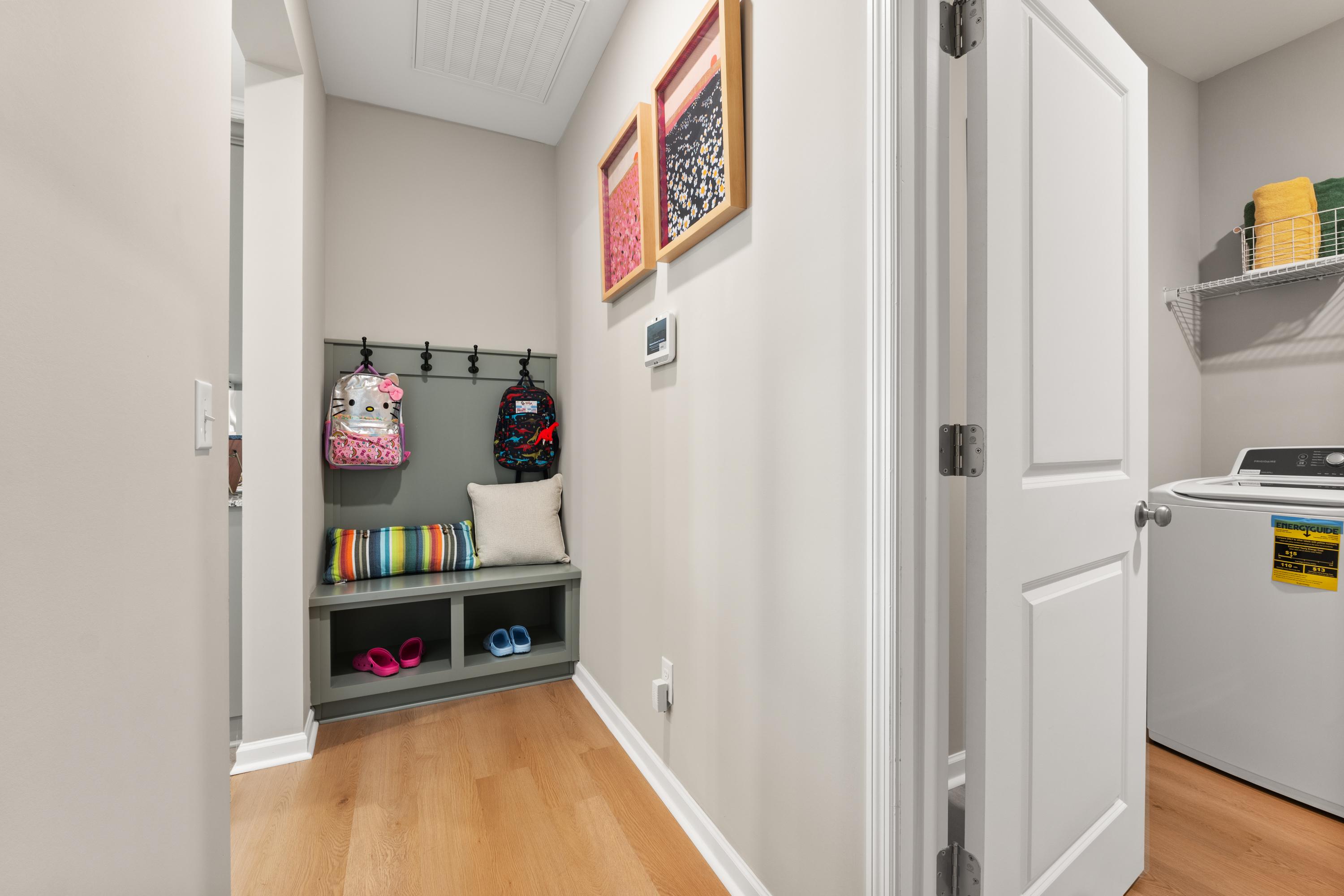 Spacious mudroom with built-in bench, backpack hooks, pink shoes, and laundry nook at The Meadows at Hampton Cove in Owens Cross Roads, Alabama
