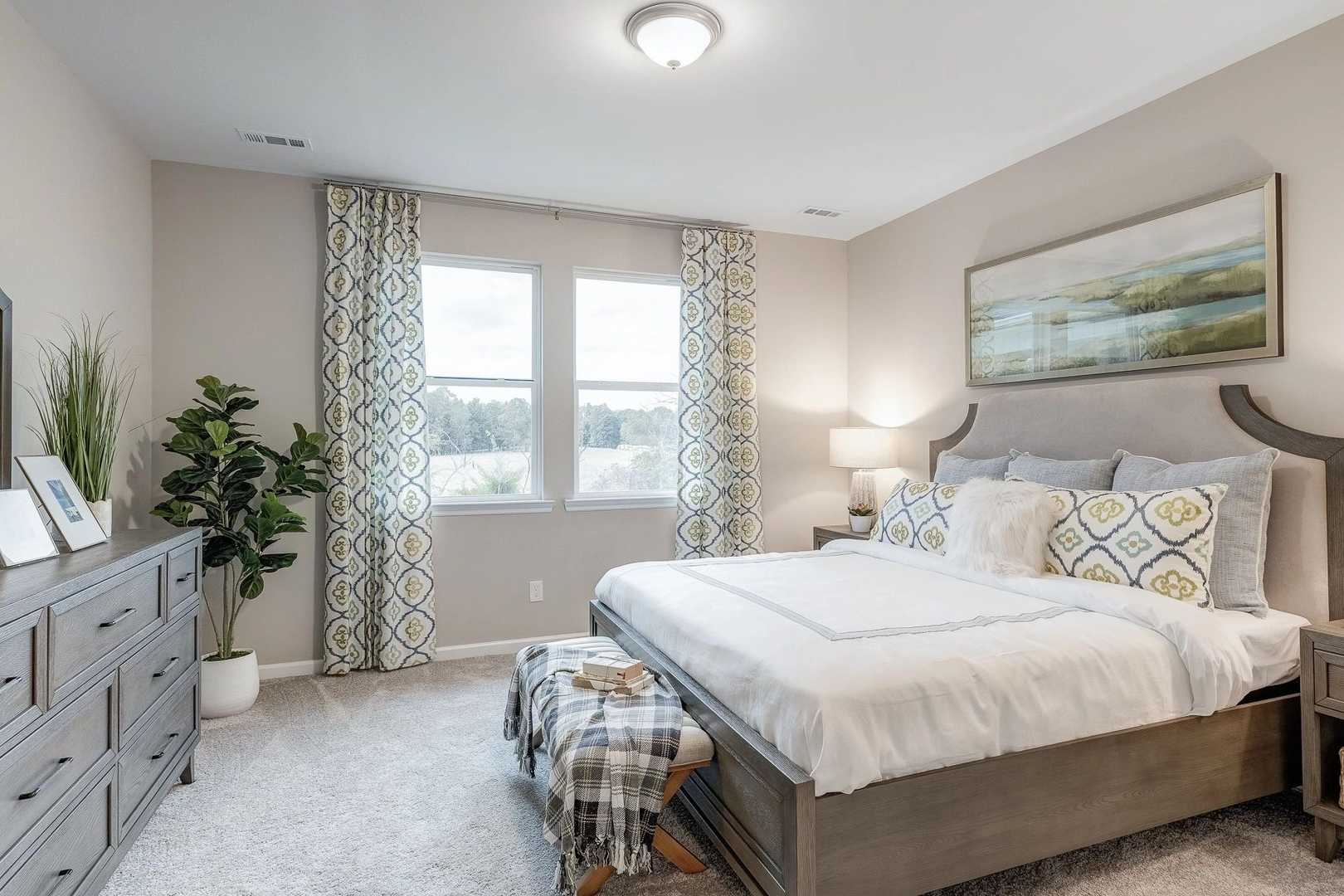 Spacious primary bedroom at Carroll Green in Harvest Alabama with king bed neutral tones plants and large windows