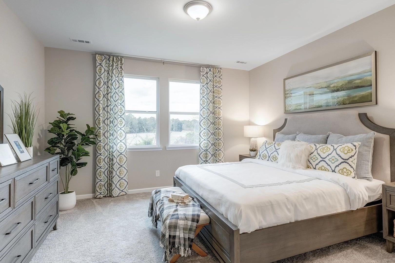 Spacious primary bedroom at Carroll Green in Harvest Alabama with king bed neutral tones plants and large windows