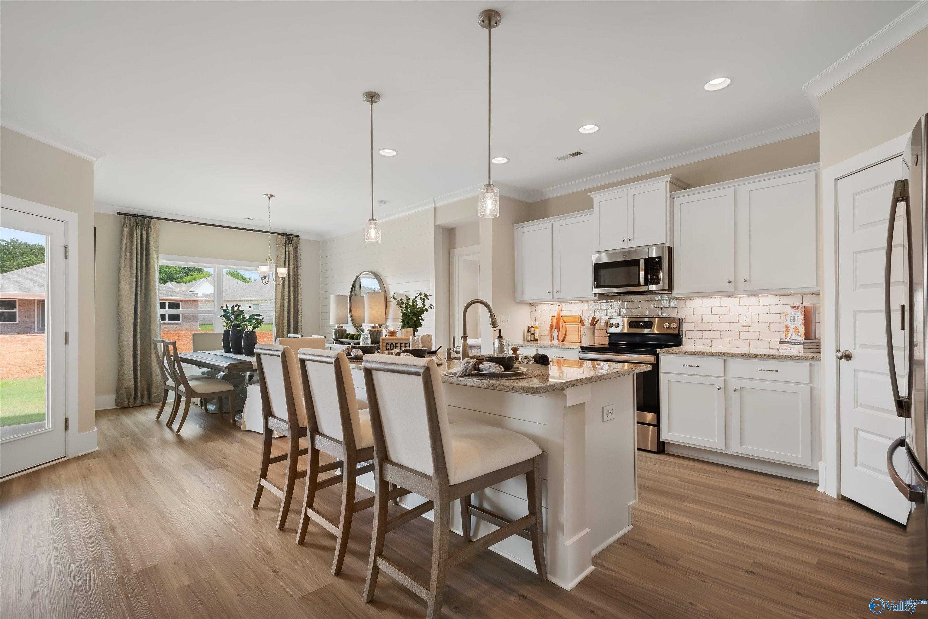 Open-concept kitchen with white cabinets, stainless appliances, large island, and dining area in Davidson Homes The Everett, New Market, Alabama