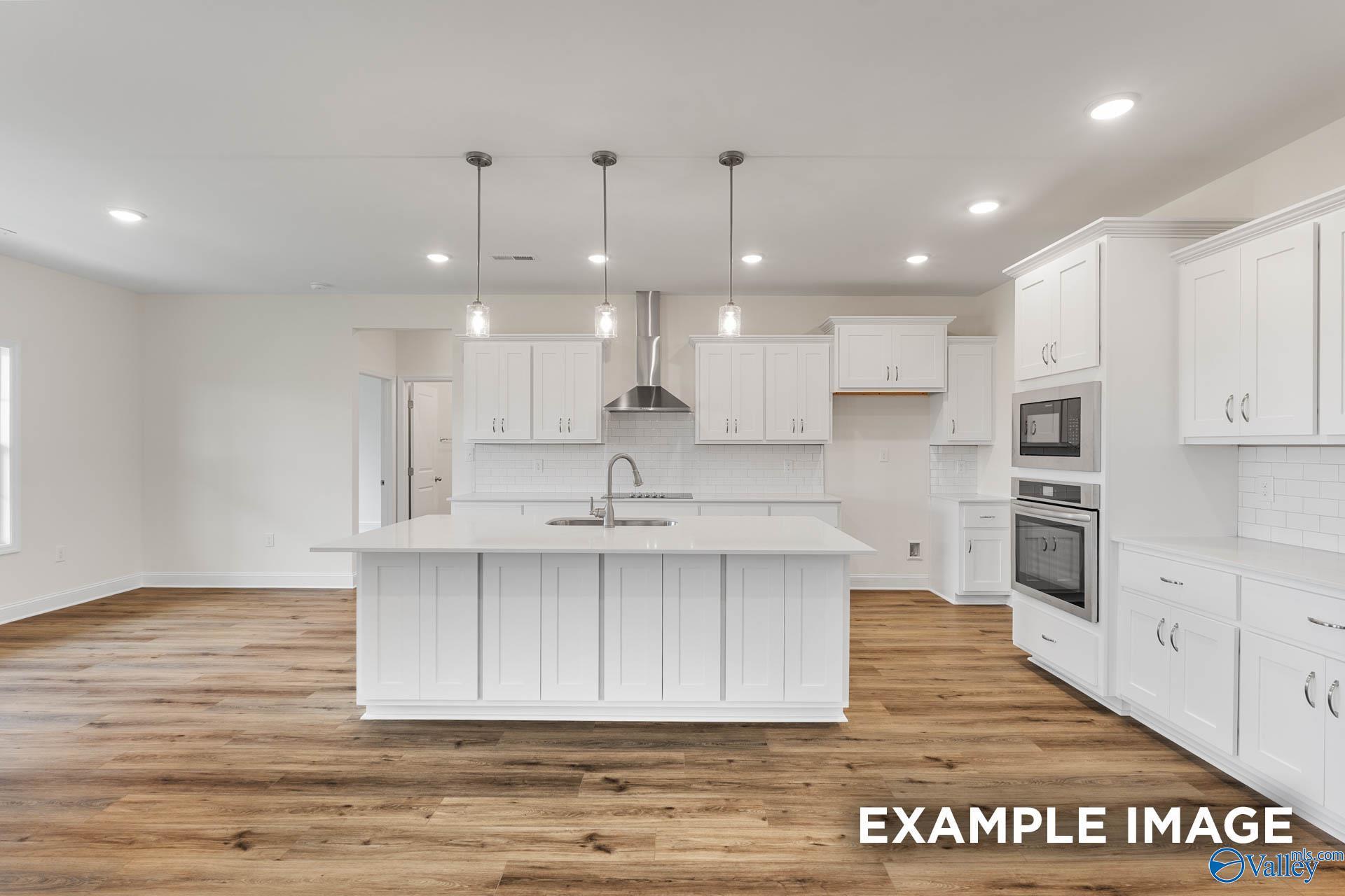 Modern white kitchen with large island, stainless appliances, pendant lights, and hardwood floors in Davidson Homes The Emory, Toney, Alabama