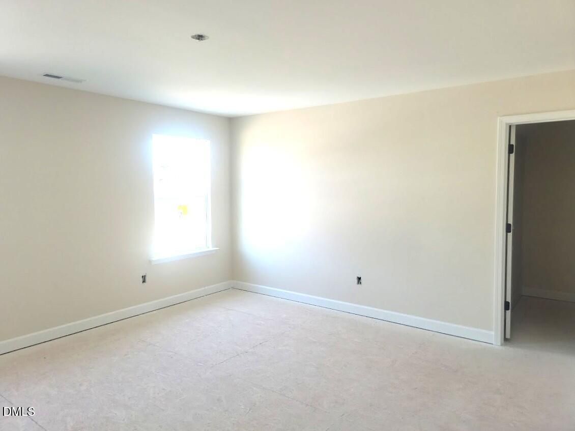 Bright empty bedroom with beige walls, carpeted floor, and natural window light in Davidson Homes The Cypress B II, Angier, NC