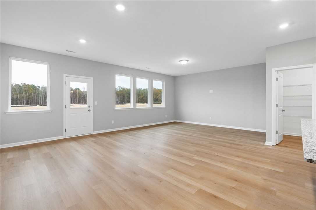 Spacious open living area with light oak floors, large windows overlooking woods, and white doors in The Luna B home, Opelika