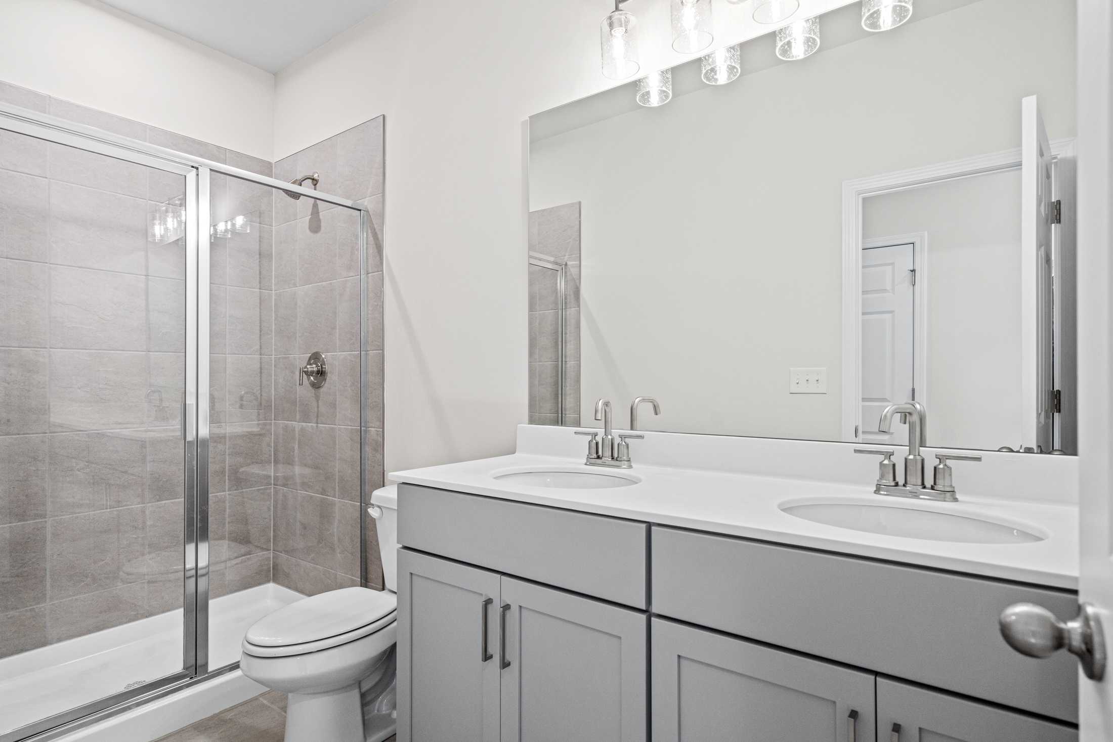 Spacious master bathroom in The Glenwood A by Davidson Homes, featuring double gray vanity, glass shower enclosure, and tiled walls
