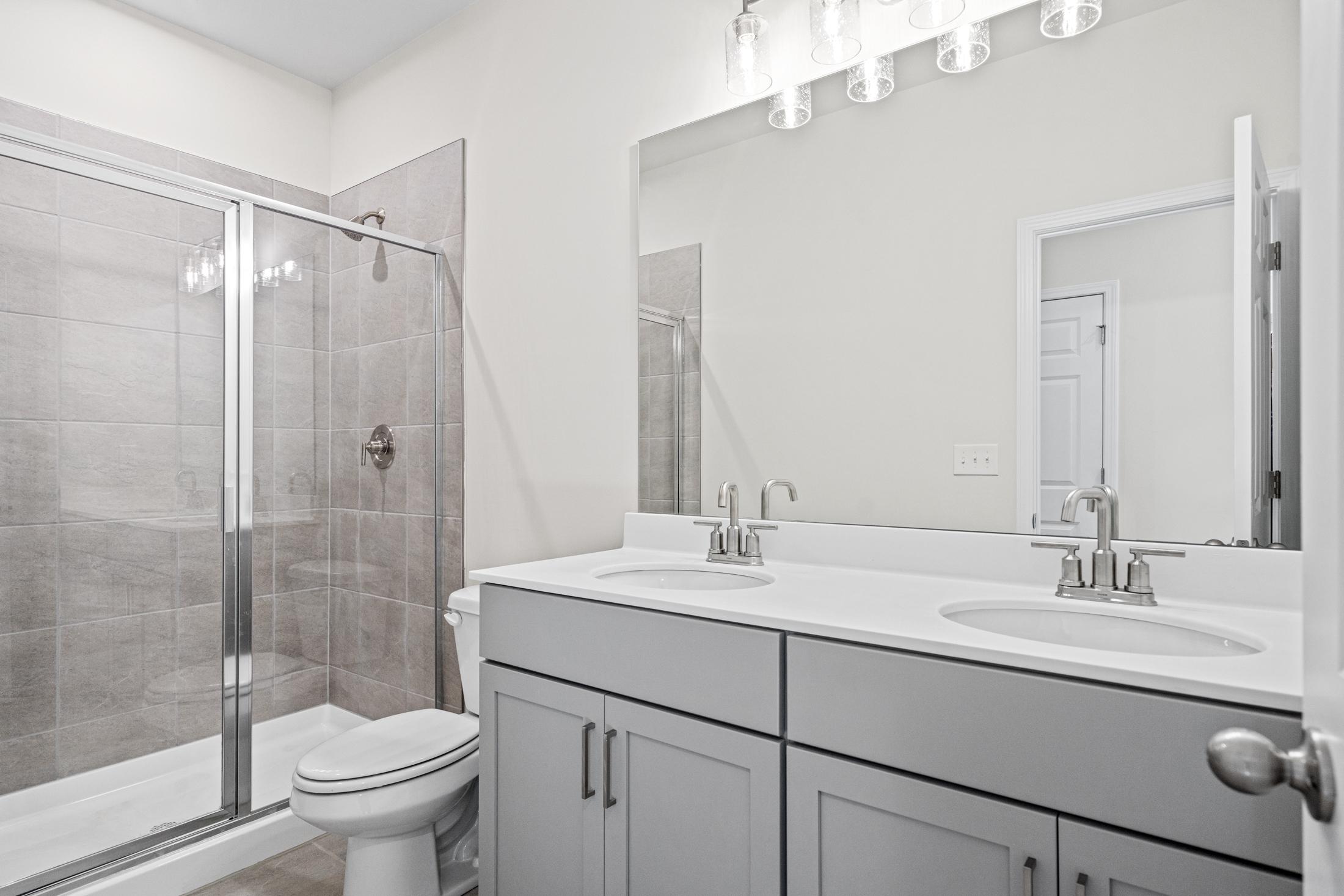 Spacious master bathroom in The Glenwood A by Davidson Homes, featuring double gray vanity, glass shower enclosure, and tiled walls