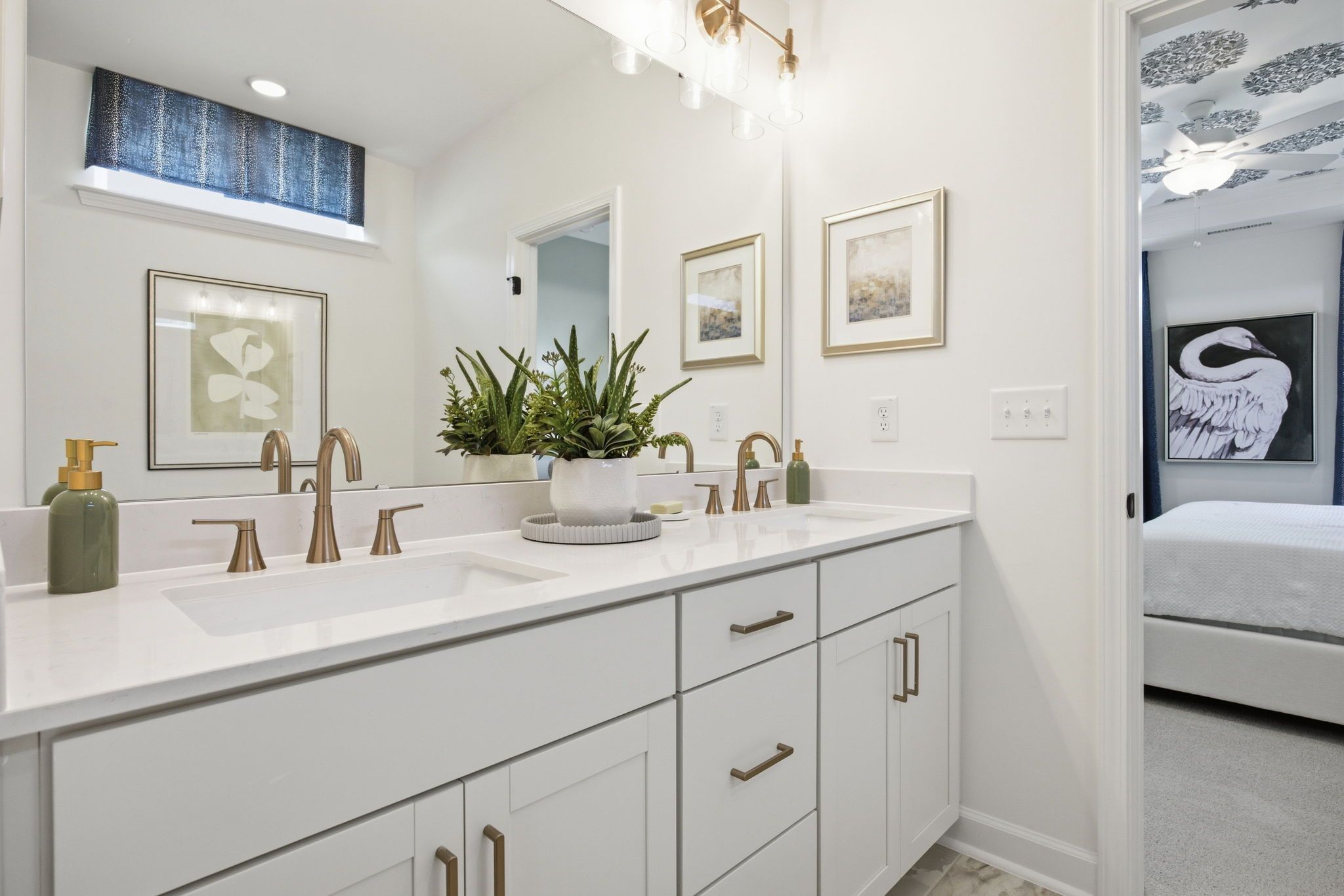 Modern primary bathroom in The Ashport featuring dual vanity, quartz countertops, and brass fixtures with master suite view.
