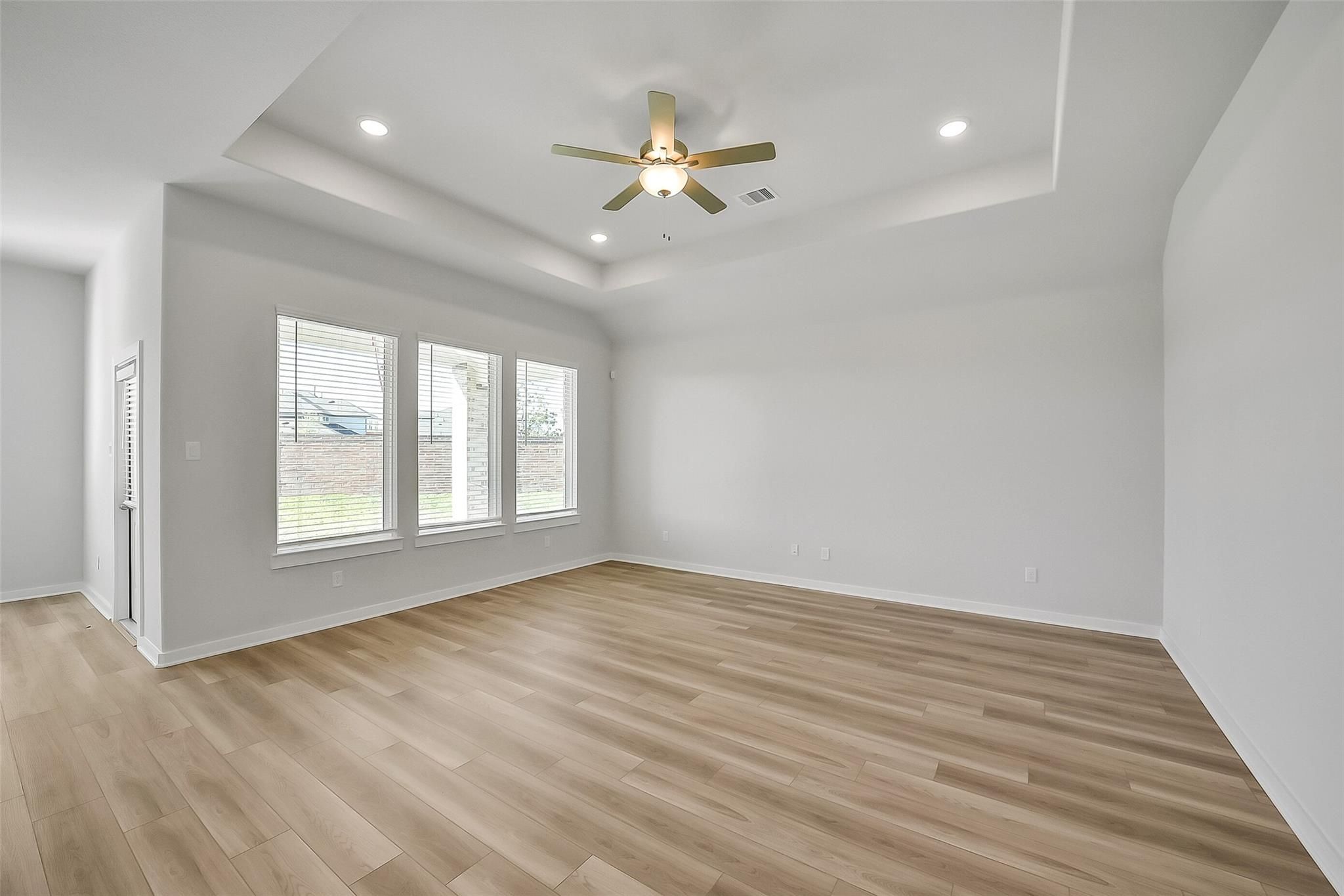 Bright living room with light wood floors, large triple windows, ceiling fan and recessed lights in Davidson Homes The Acadia A, Sunterra, Katy, Texas