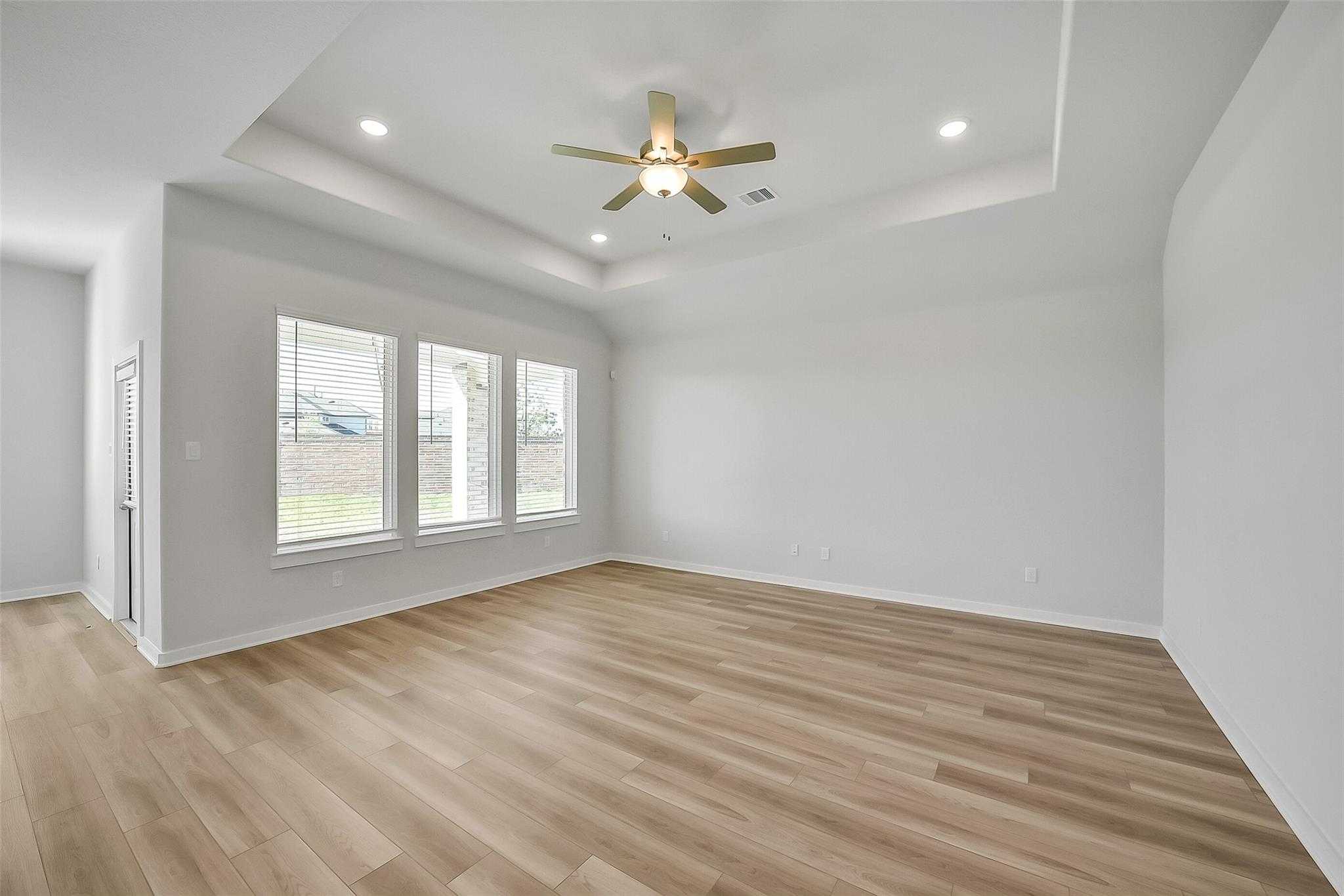Bright living room with light wood floors, large triple windows, ceiling fan and recessed lights in Davidson Homes The Acadia A, Sunterra, Katy, Texas