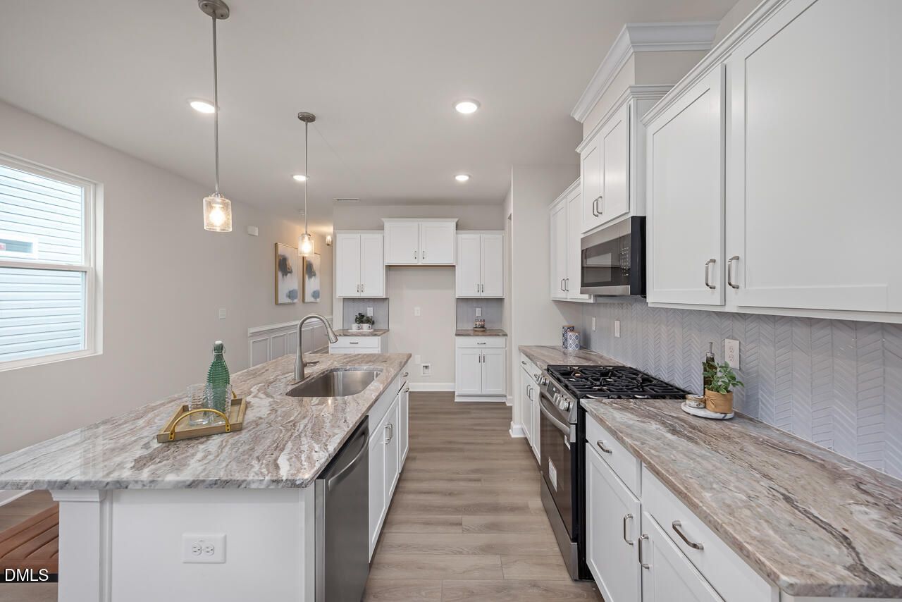 Modern kitchen with white shaker cabinets, veined quartz island, stainless appliances in The Carter C home, Lillington NC