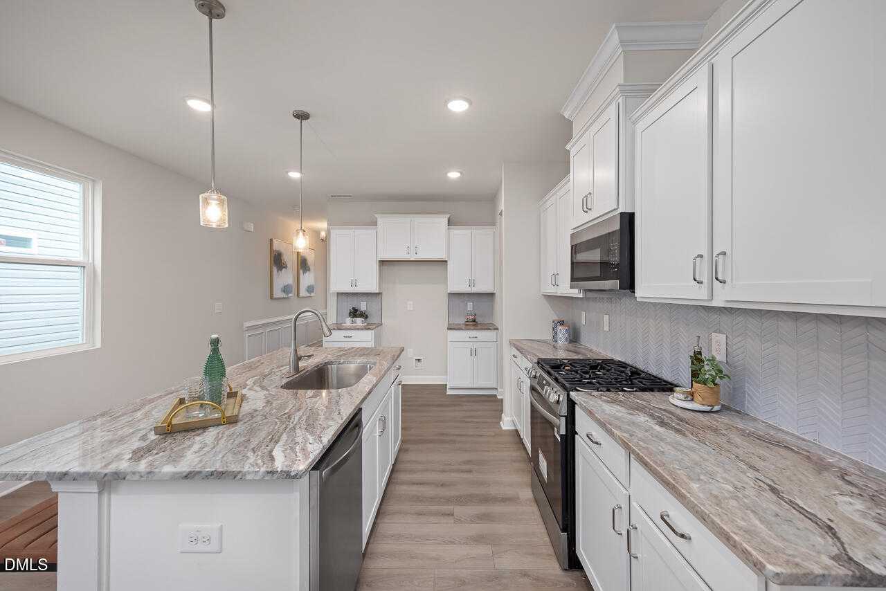 Modern kitchen with white shaker cabinets, veined quartz island, stainless appliances in The Carter C home, Lillington NC