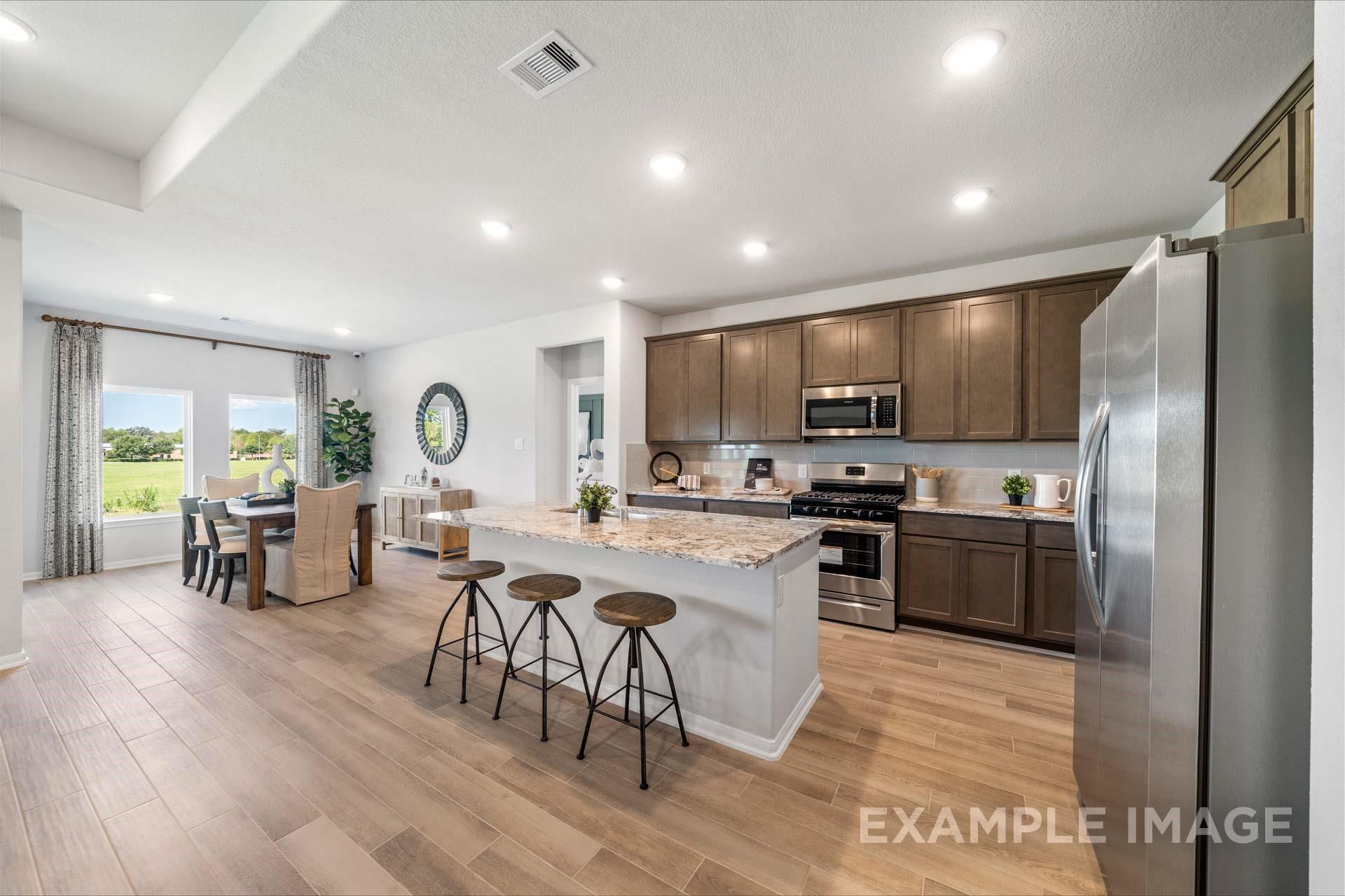Open-concept kitchen with granite island, stainless appliances, and wood-look tile flooring in Davidson Homes Acadia A, Texas City