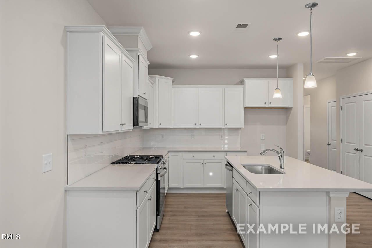 Bright white kitchen with island sink, subway tile backsplash, gas range, and pendant lights in Davidson Homes The Graham, Fuquay-Varina, NC