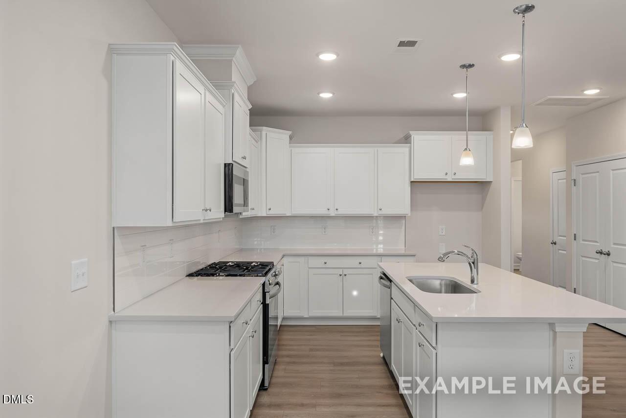 Bright white kitchen with island sink, subway tile backsplash, gas range, and pendant lights in Davidson Homes The Graham, Fuquay-Varina, NC