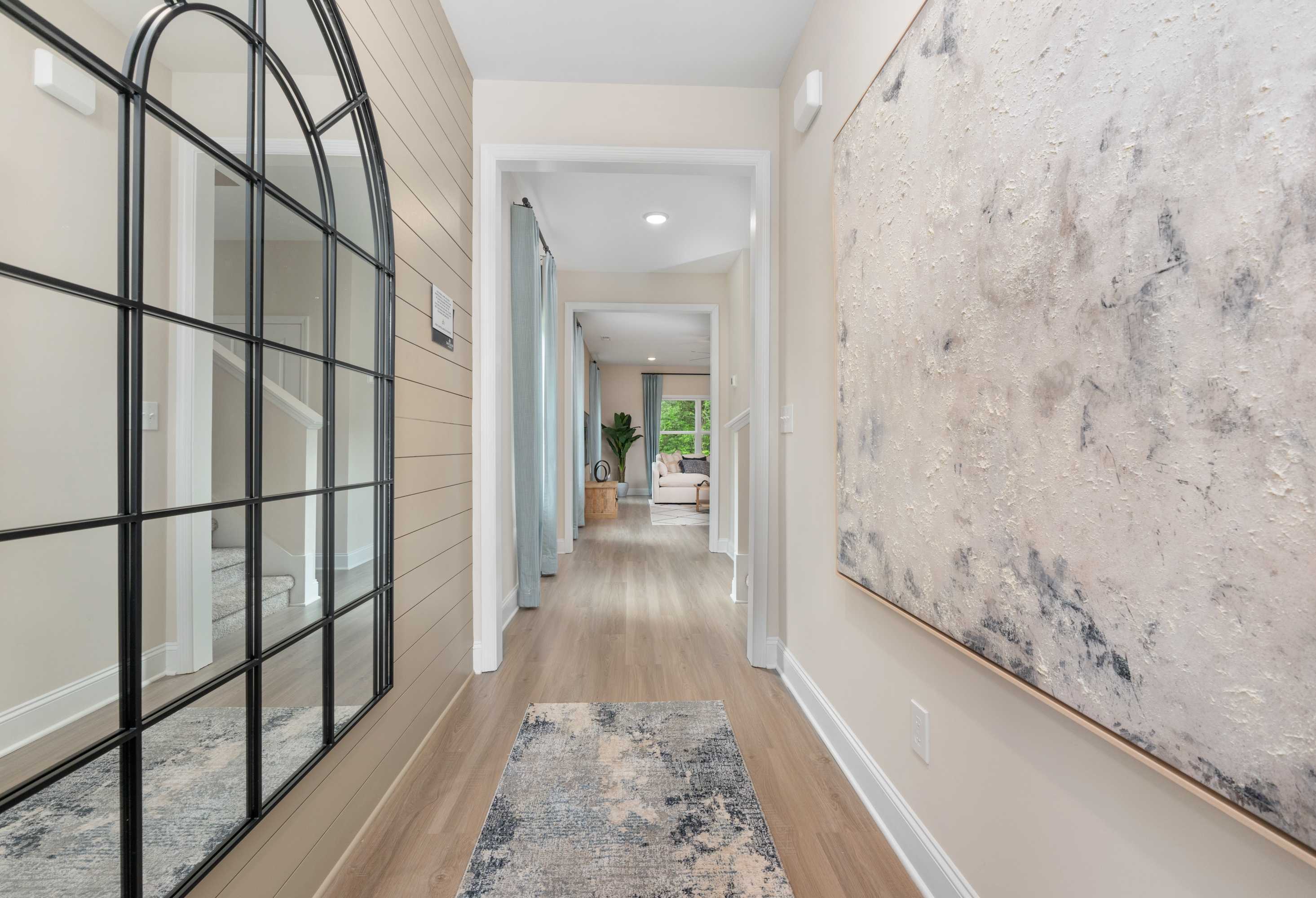 Spacious entry hallway in The Camden home with arched black mirror, beige shiplap walls, wood floors, and abstract art