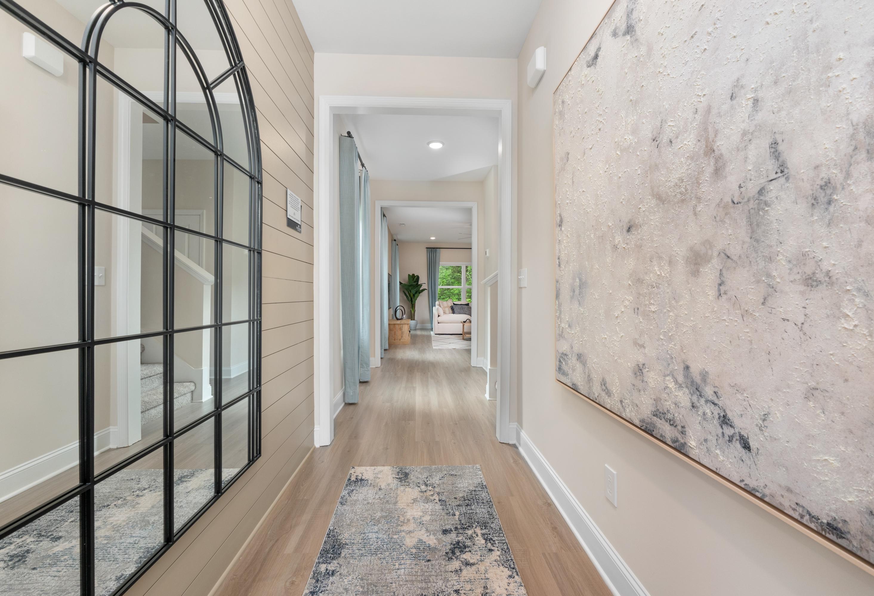 Spacious entry hallway in The Camden home with arched black mirror, beige shiplap walls, wood floors, and abstract art