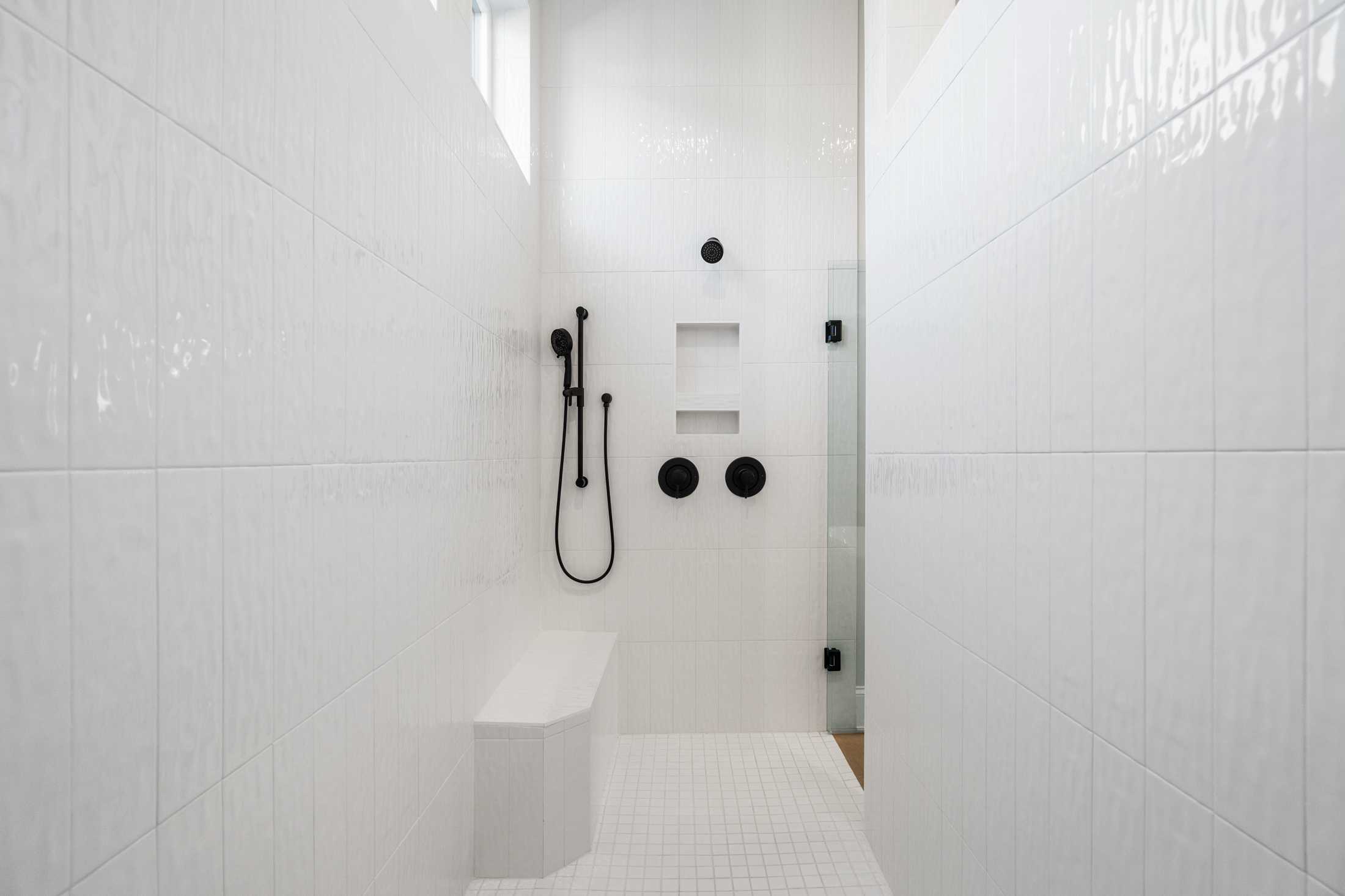Modern white subway tile walk-in shower with black rain showerhead, handheld sprayer, bench, and niche in The Seaside master bath