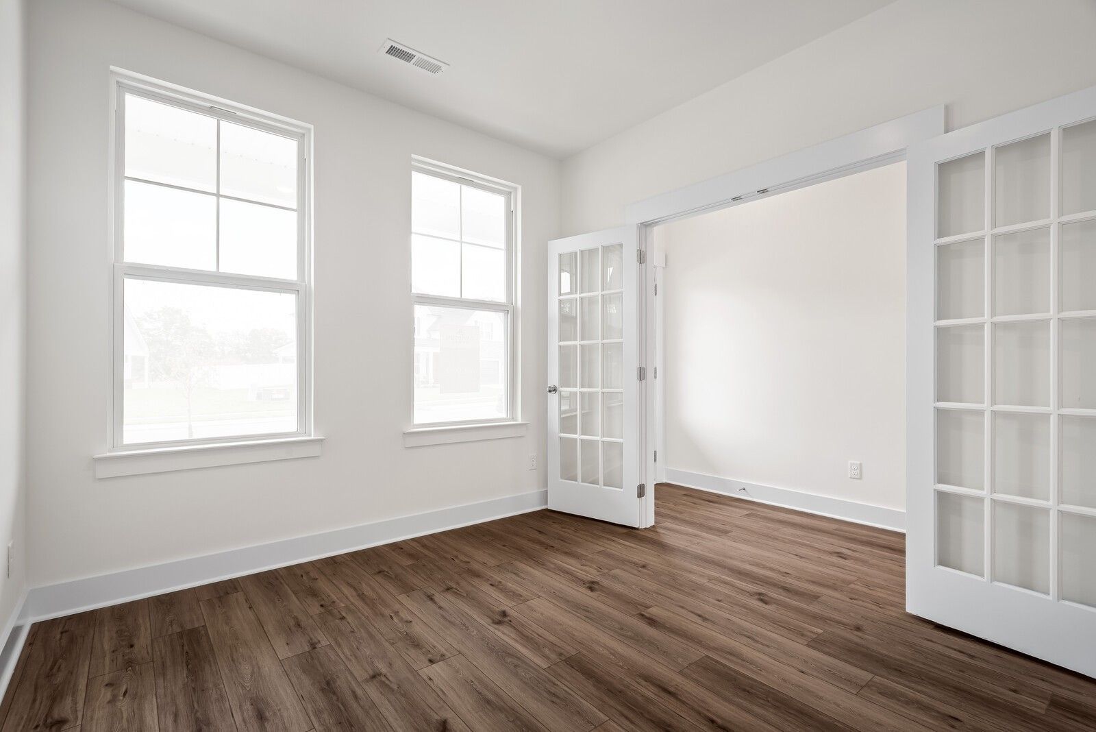 Bright living room with large windows, open French doors, and hardwood floors in The Logan C home, Gallatin, Tennessee