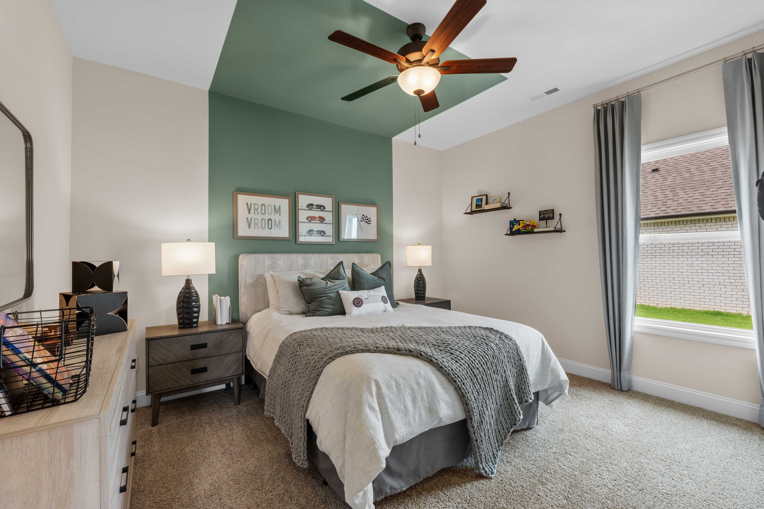 Cozy master bedroom in The Daphne plan with green accent wall, gray bedding, ceiling fan, and window views