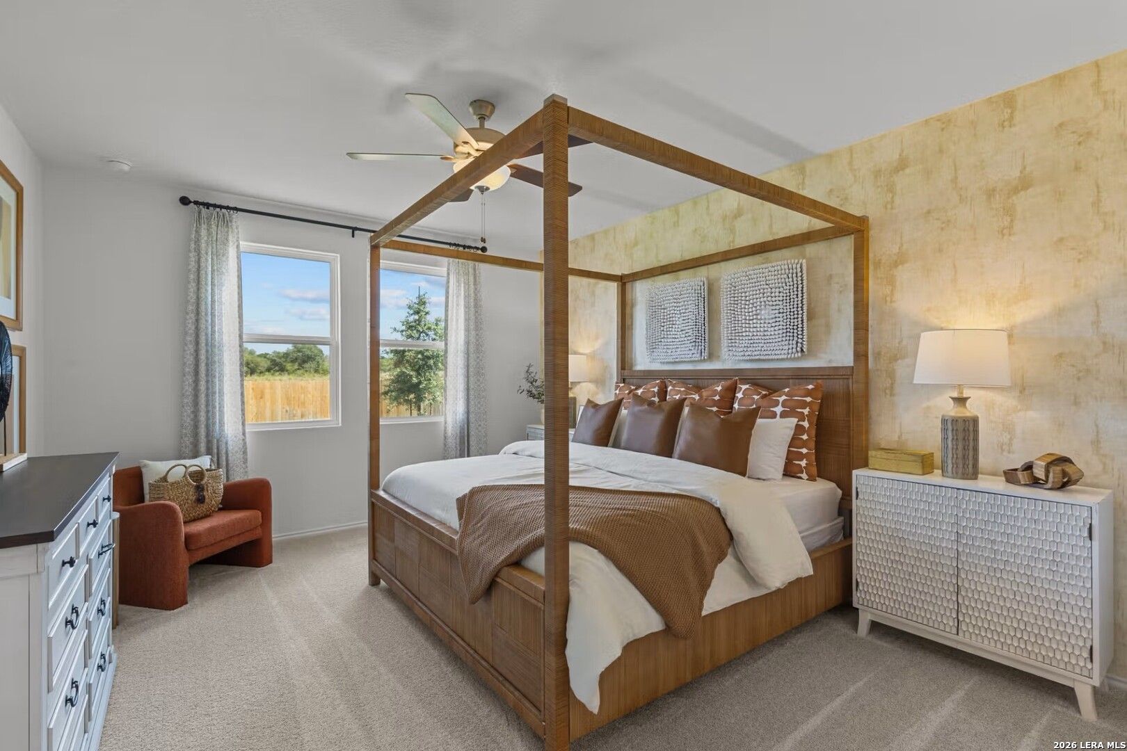 Elegant master bedroom with wooden four-poster bed, orange pillows, textured walls, and window overlooking backyard in Davidson Homes The Daphne K, Bricewood San Antonio