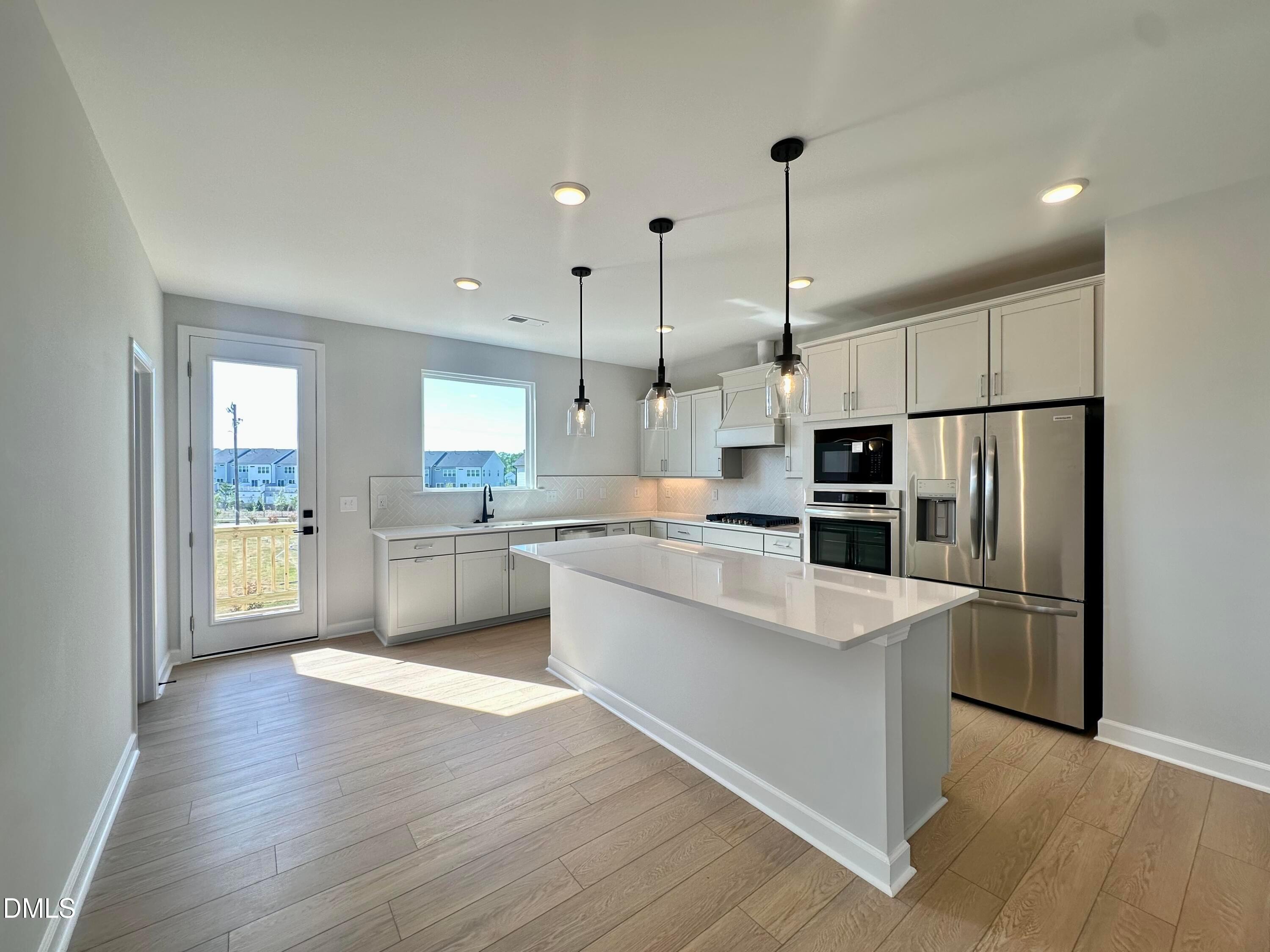 Modern white kitchen with quartz island, stainless steel appliances, pendant lights, and French doors to patio in Davidson Homes The Avery, Knightdale, NC