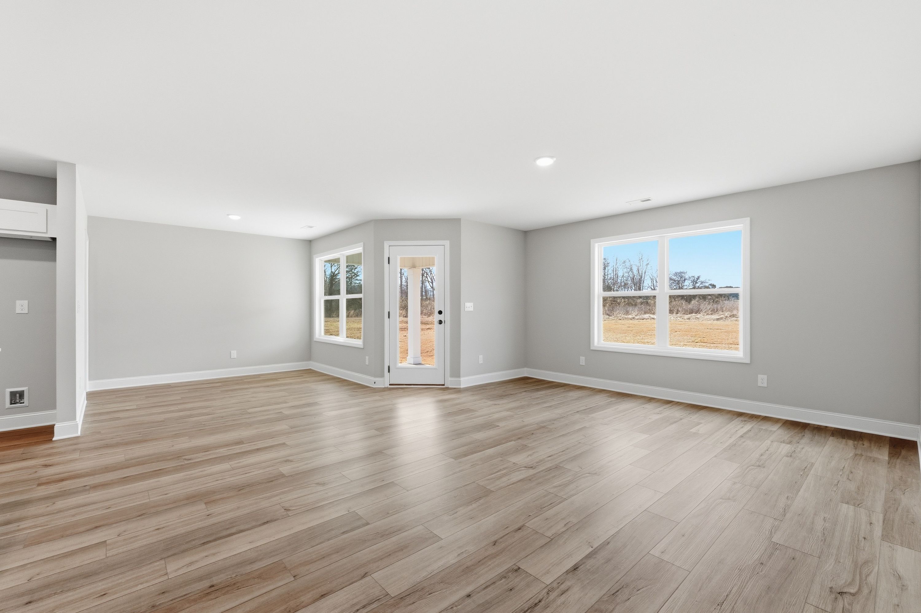 Spacious open living room in The Daphne V home with gray walls, hardwood floors, and large windows