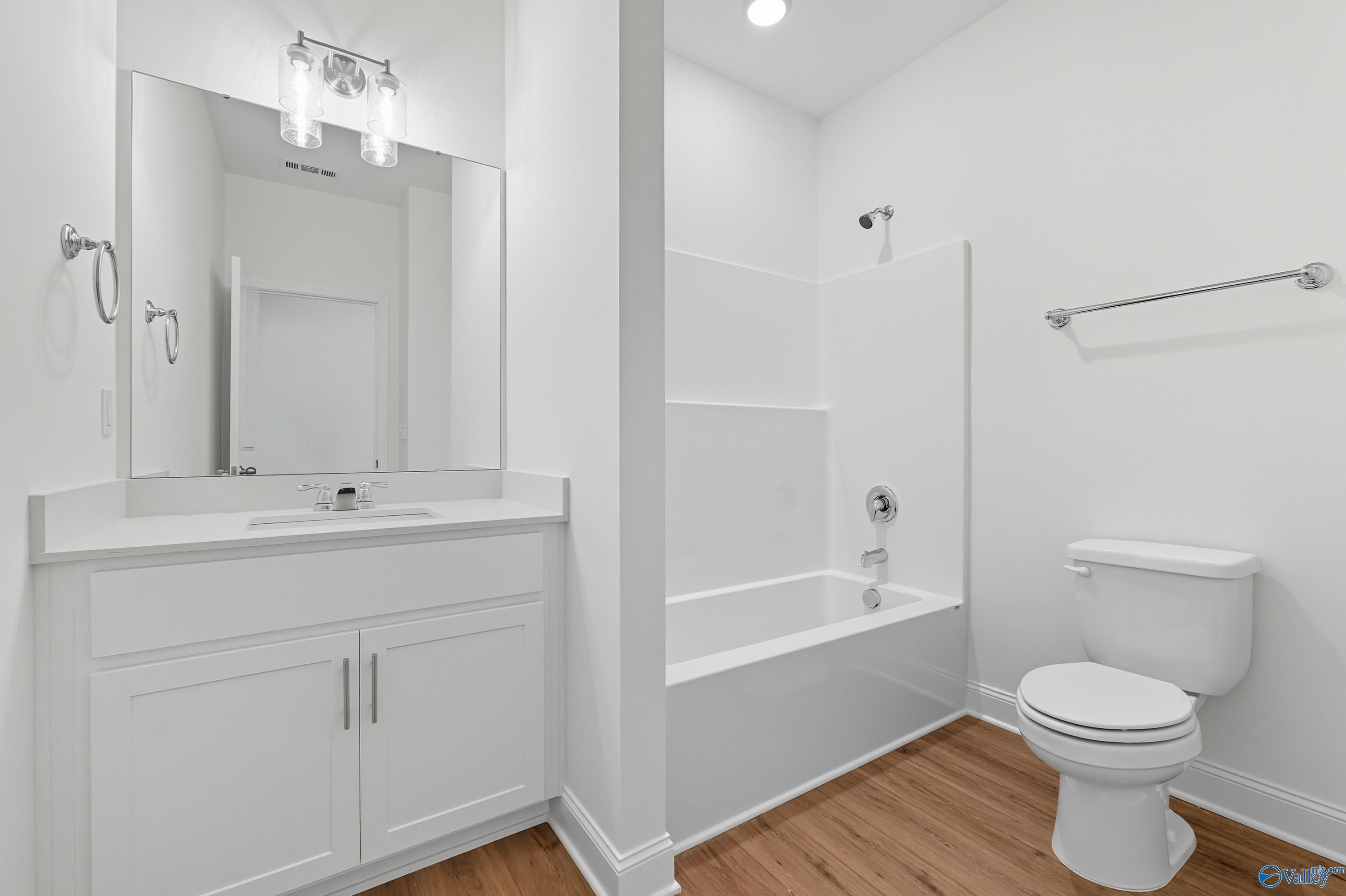 Modern white guest bathroom with bathtub-shower combo, vanity sink, and hardwood floors in Davidson Homes The Everett, Meridianville, Alabama