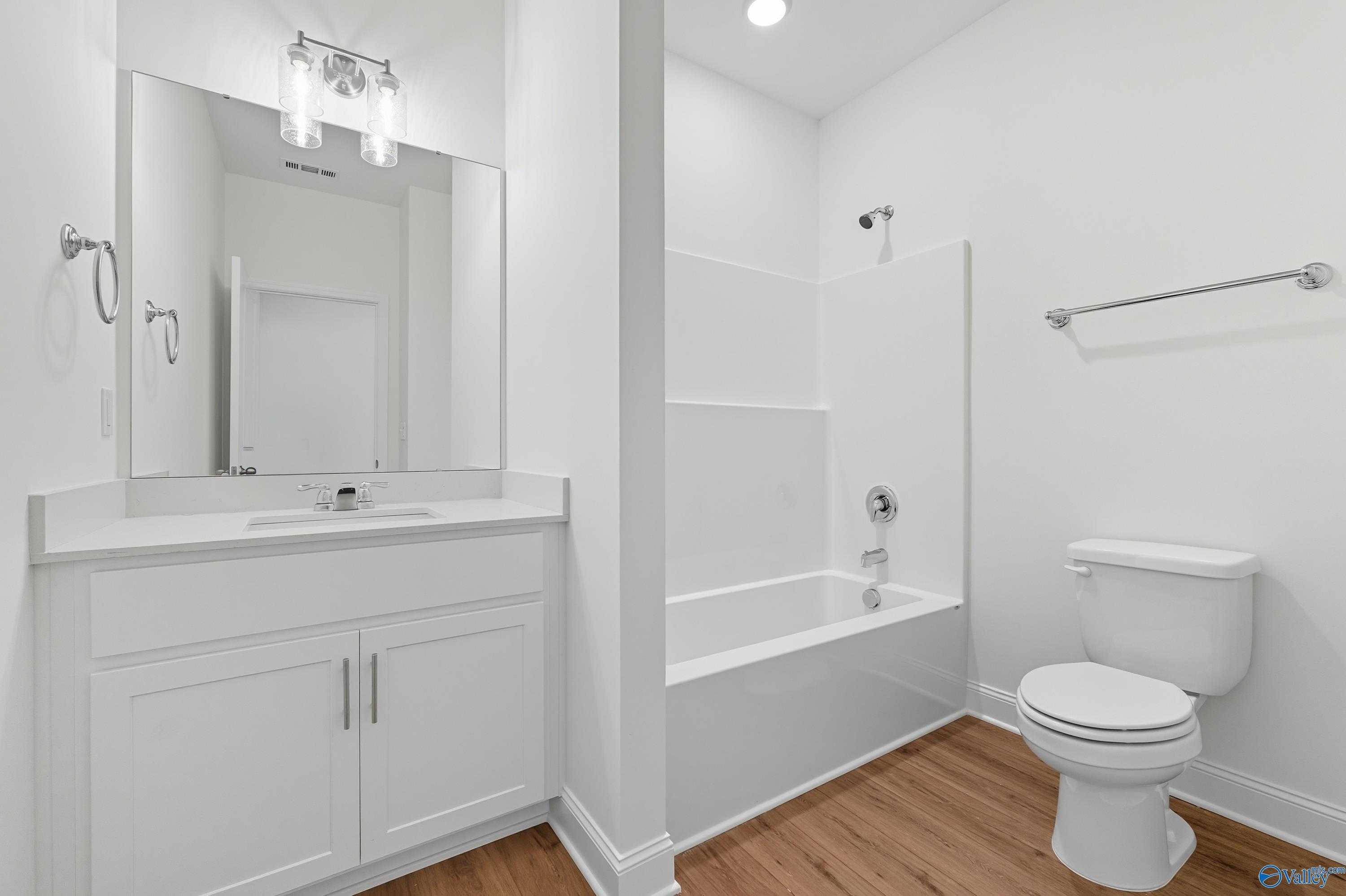 Modern white bathroom featuring bathtub-shower combo, vanity, mirror, and hardwood floors in Davidson Homes The Everett, Meridianville, Alabama