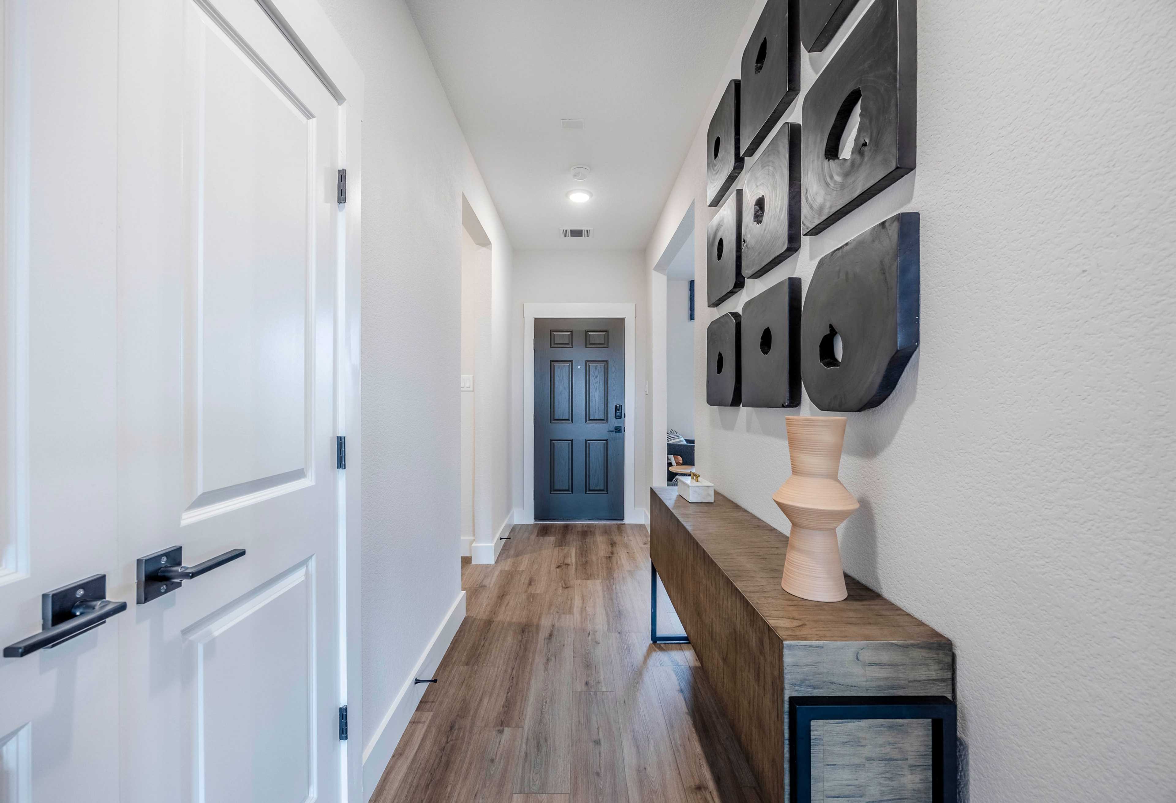 Modern hallway in The Rockford home by Davidson Homes, featuring white walls, hardwood floors, black square wall art, vase on console table