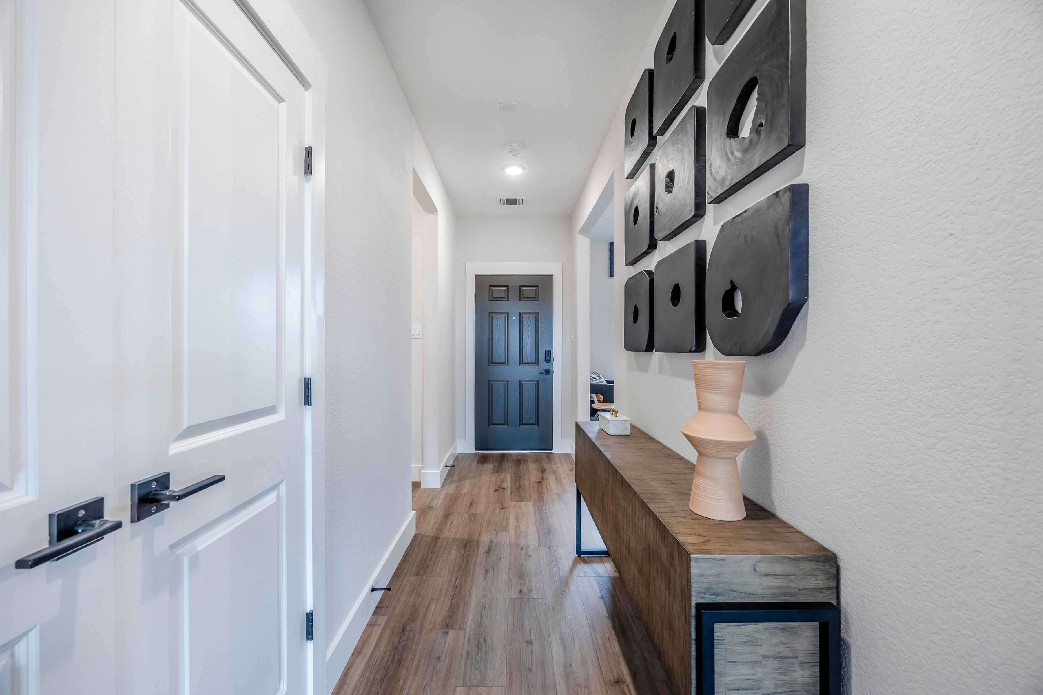 Modern hallway in The Rockford home by Davidson Homes, featuring white walls, hardwood floors, black square wall art, vase on console table