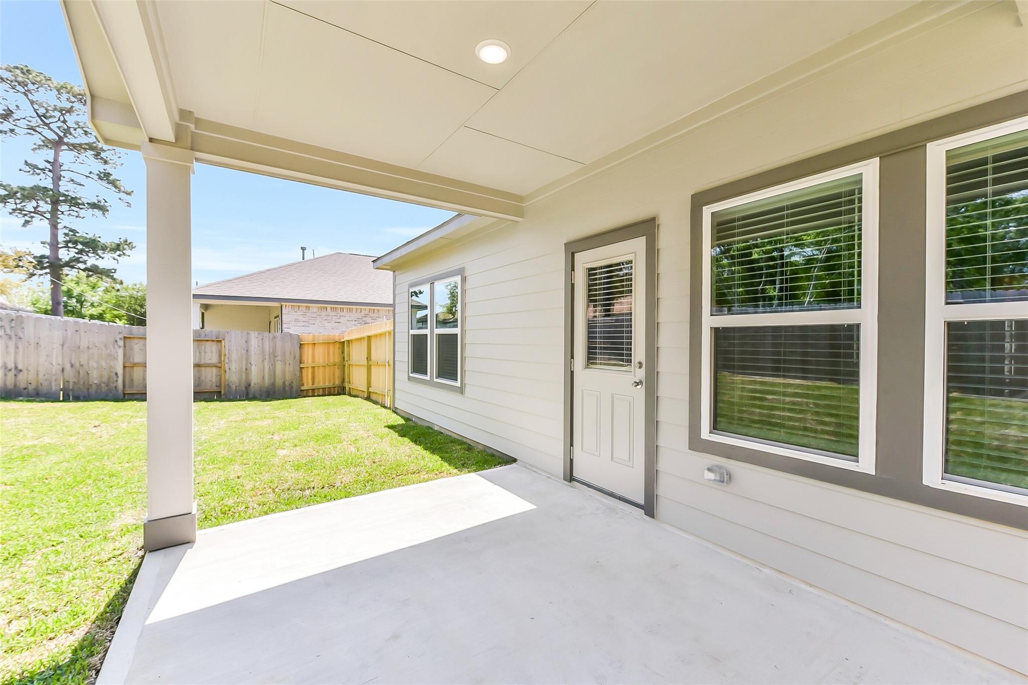 Covered back patio with green lawn, wooden fence, and beige exterior in Davidson Homes The Brazos E, Windmill Estates, Magnolia, Texas