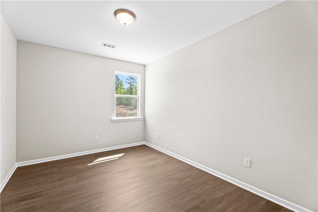 Bright bedroom with neutral walls, wood laminate floors, and window view in Evermore Homes The Orion, Cusseta, Alabama