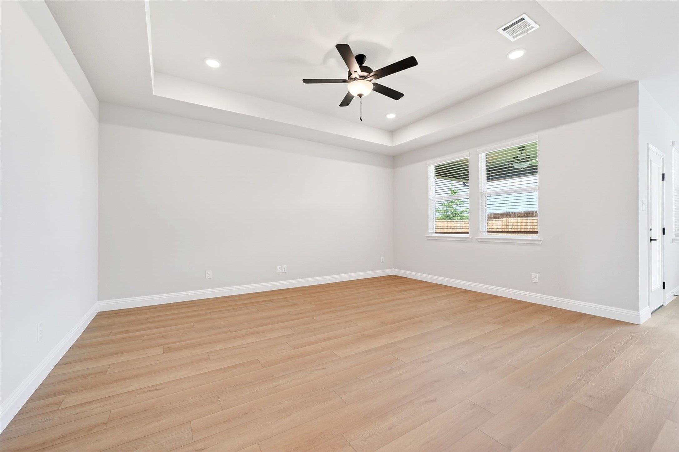 Spacious living area with tray ceiling, ceiling fan, and light wood floors in The Holly C floor plan, Anna, Texas.