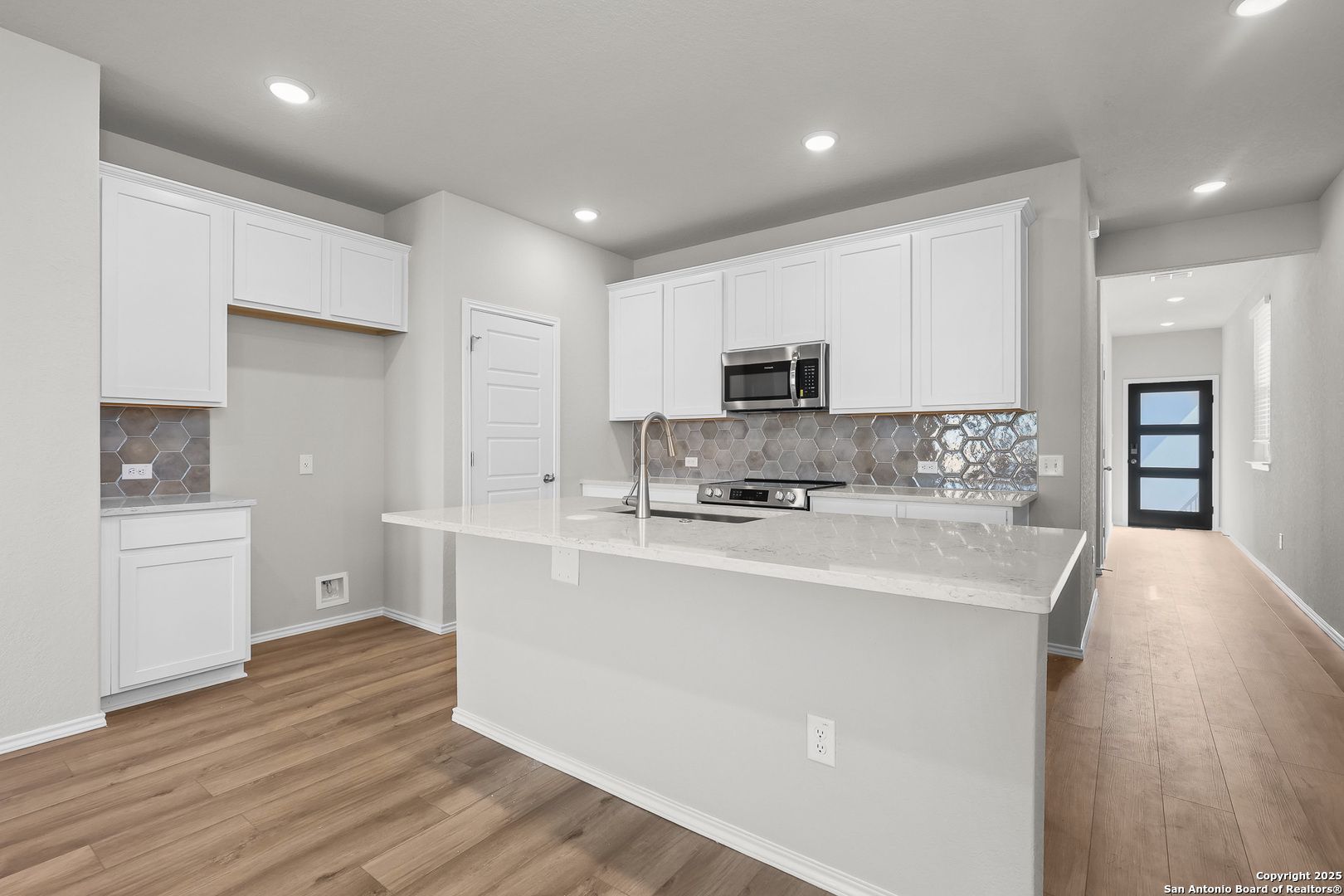 Modern white kitchen with quartz island, stainless appliances, geometric backsplash in Davidson Homes The Colorado B, San Antonio