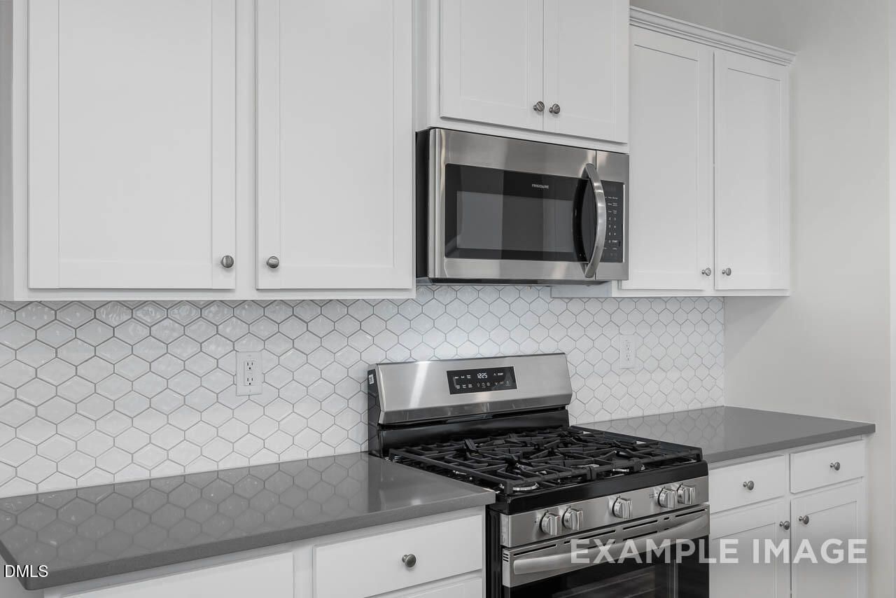 Modern kitchen with white shaker cabinets, gray quartz counters, stainless steel appliances and hexagonal backsplash in Davidson Homes Adalynn A, Lillington, NC