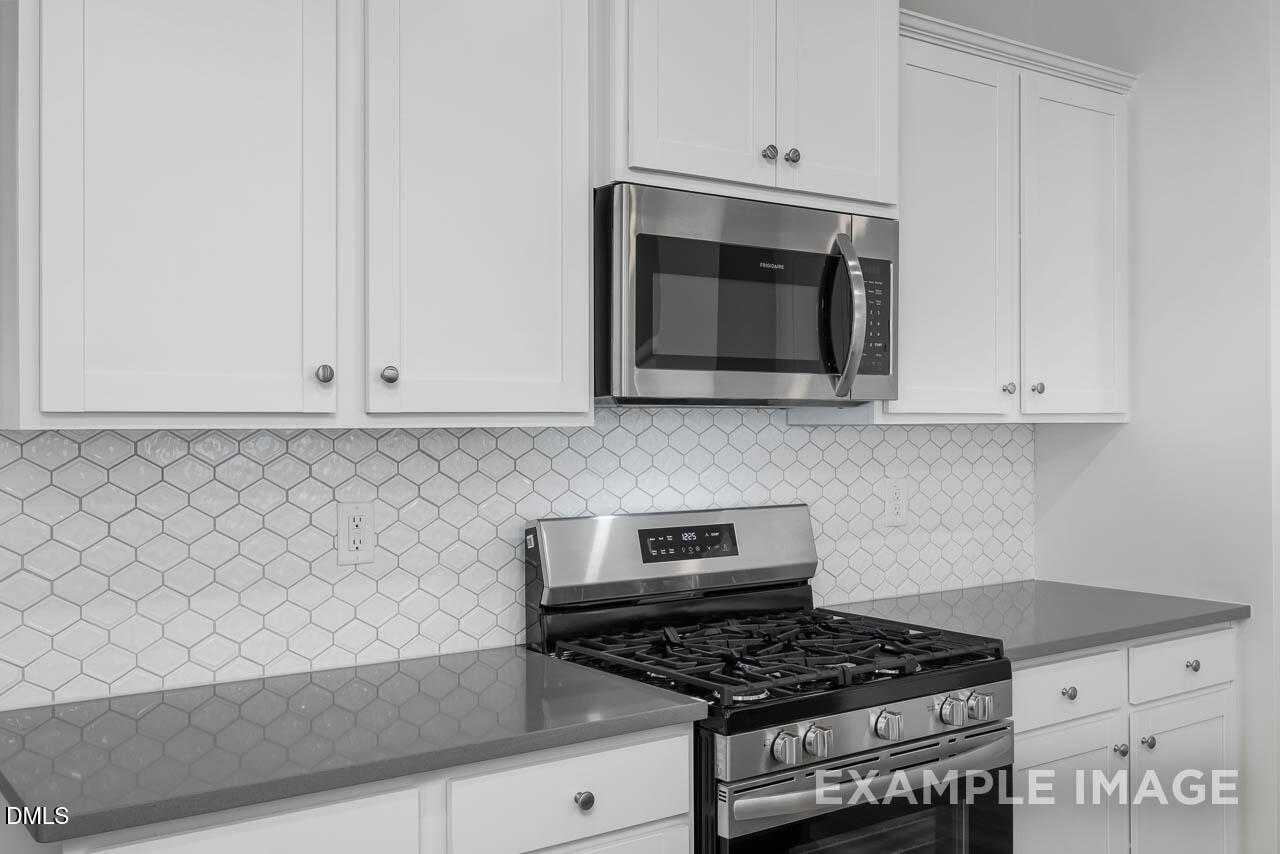 Modern kitchen with white shaker cabinets, gray quartz counters, stainless steel appliances and hexagonal backsplash in Davidson Homes Adalynn A, Lillington, NC