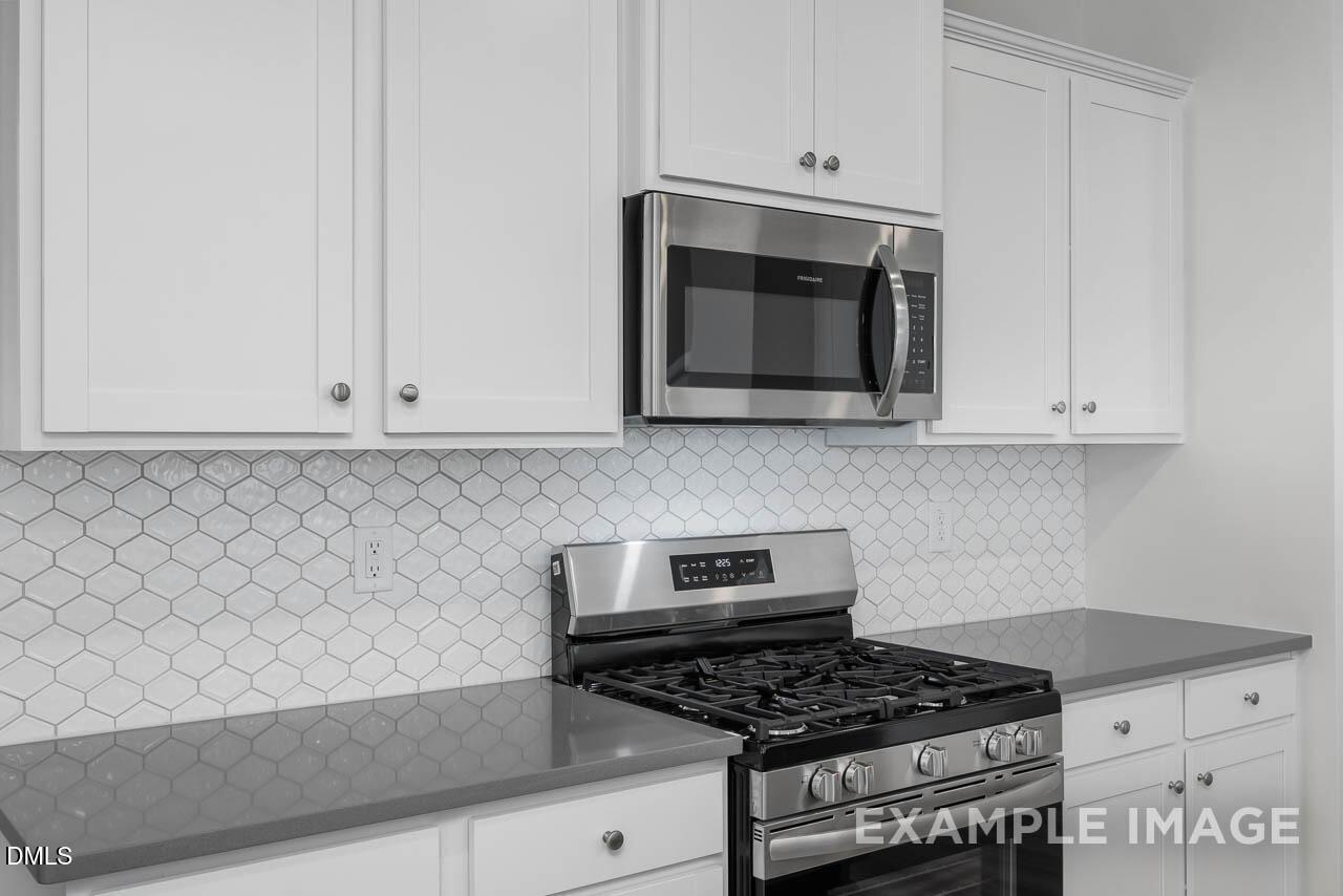 Modern kitchen with white shaker cabinets, gray quartz counters, hexagonal tile backsplash, and stainless Frigidaire appliances in The Adalynn B, Lillington NC
