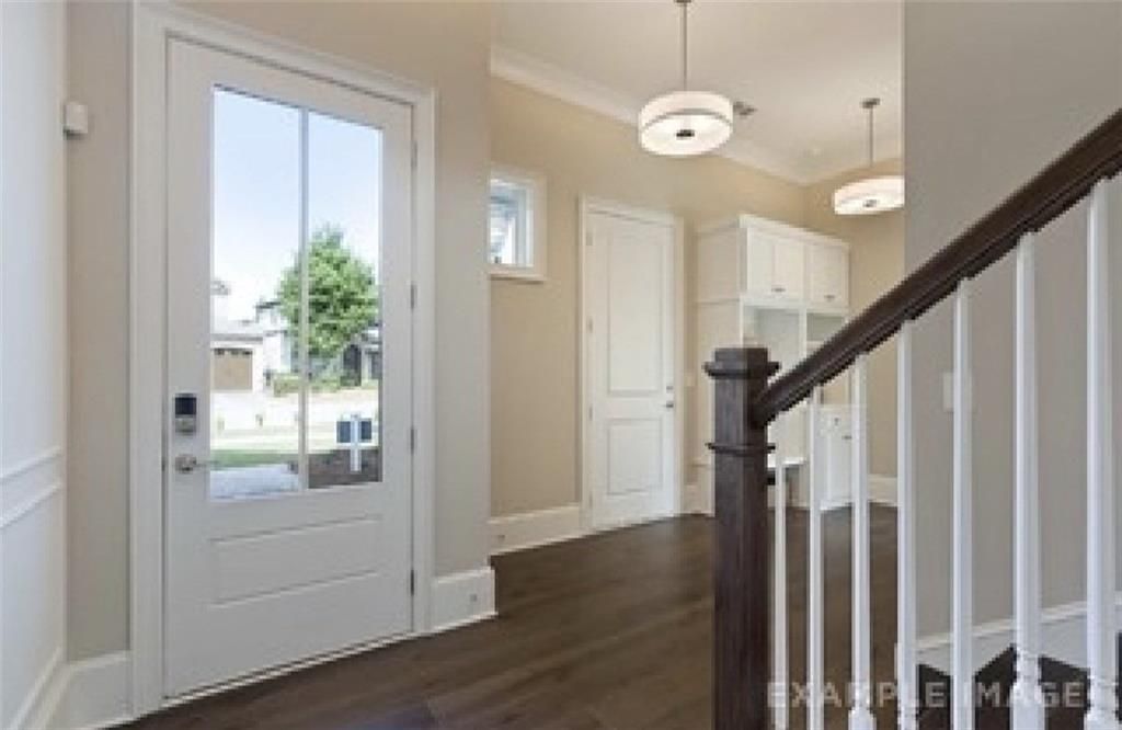 Elegant foyer with grand wooden staircase, glass-paneled front door, and pendant lights in Davidson Homes Seaside A, Woodstock, GA