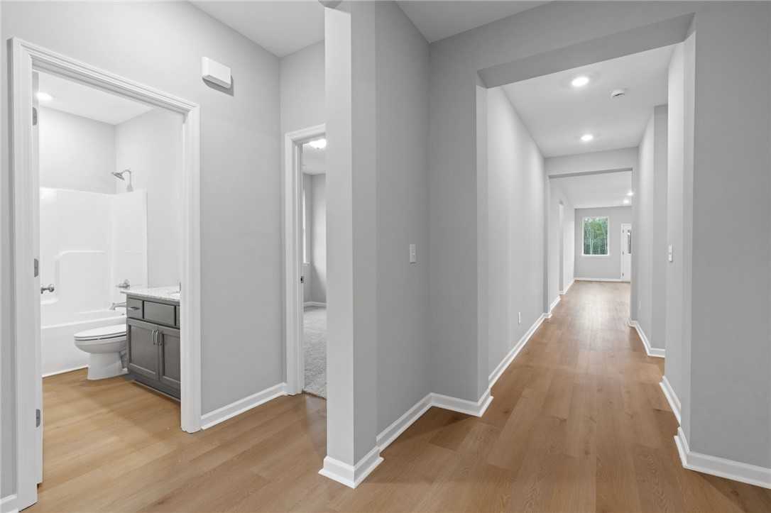 Bright hallway with hardwood floors and adjacent bathroom featuring white tub, shower, and gray vanity in The Luna B home, Opelika