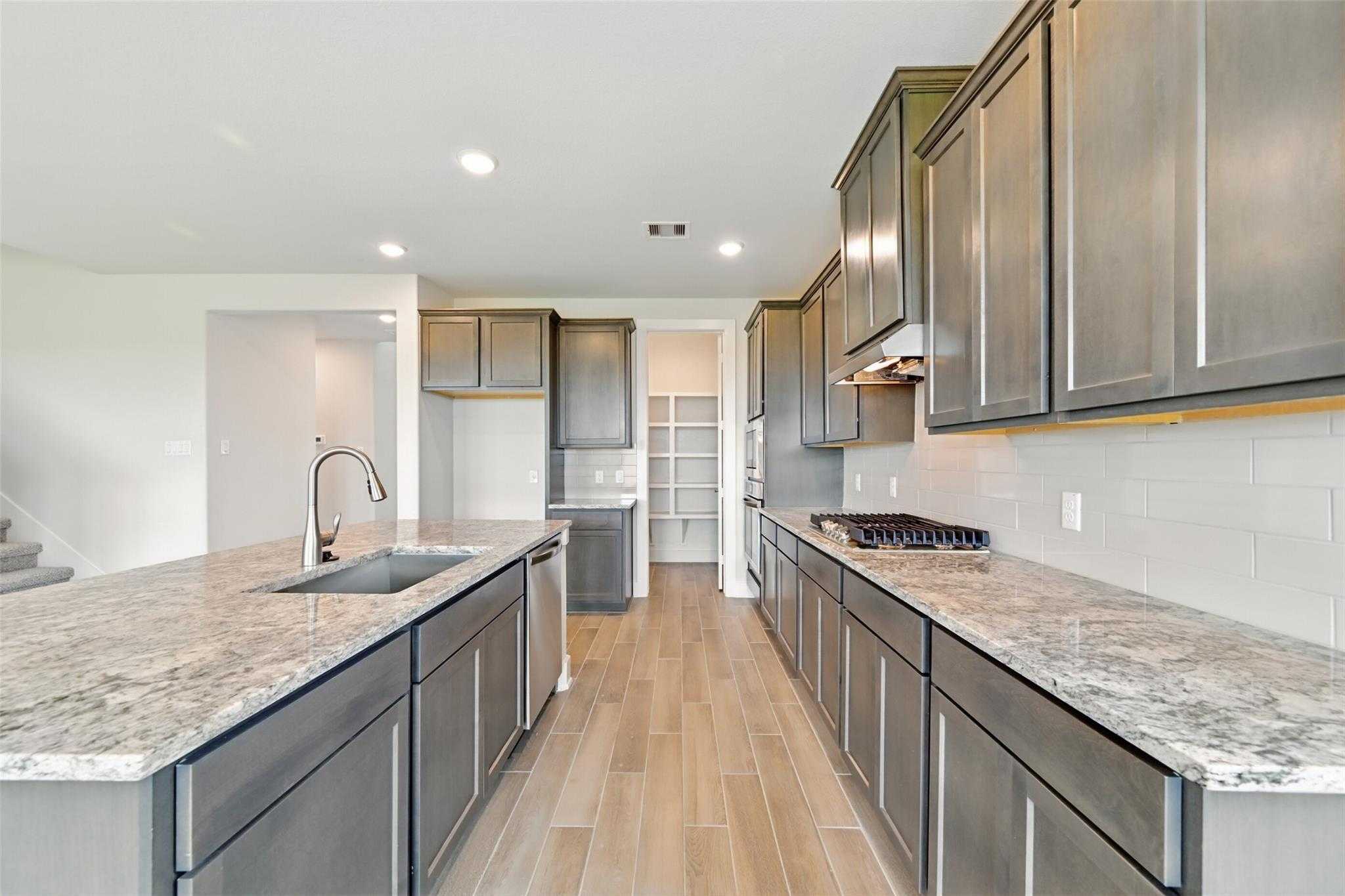 Modern kitchen with gray shaker cabinets, speckled granite island, stainless appliances and subway tile backsplash in Davidson Homes The Philip A, Lago Mar, Texas City
