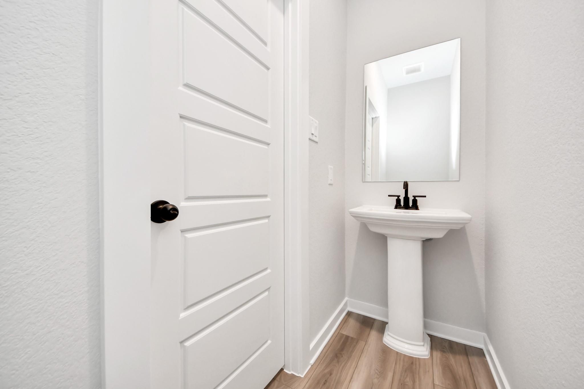 Modern powder room with pedestal sink, matte black faucet, and mirror in The Sorrento E floor plan, Sundance Cove, Crosby.