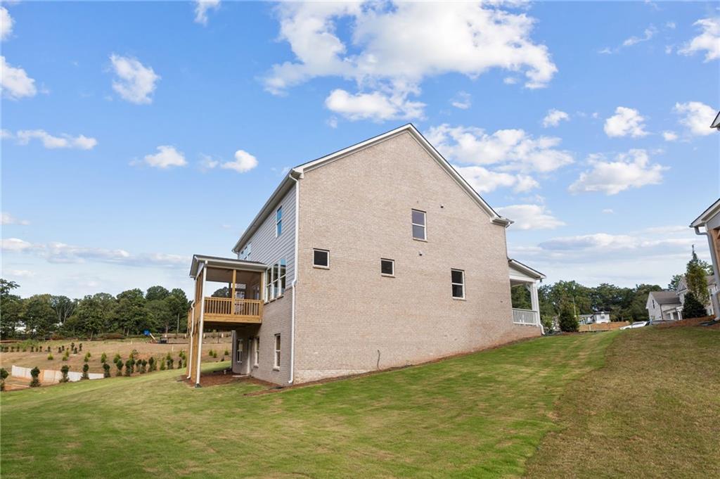 Two-story beige brick Hickory B home with upper deck and sloped green yard in Melody Lakeside Estates, Buford, Georgia