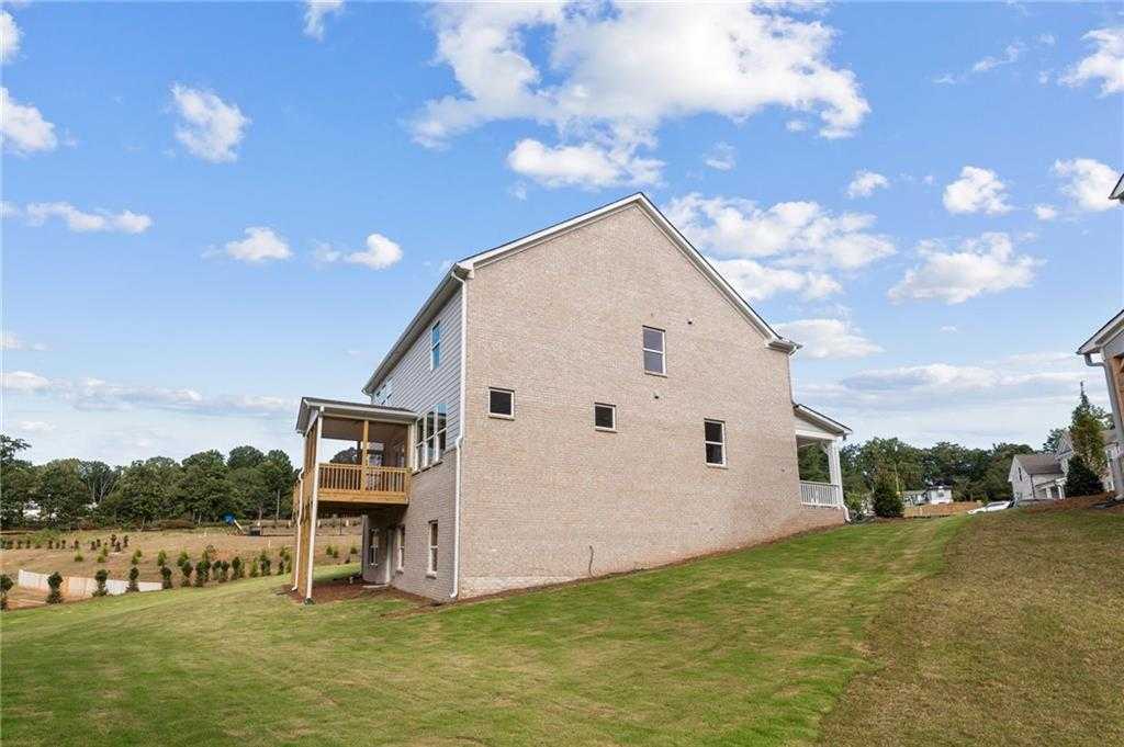 Two-story beige brick Hickory B home with upper deck and sloped green yard in Melody Lakeside Estates, Buford, Georgia