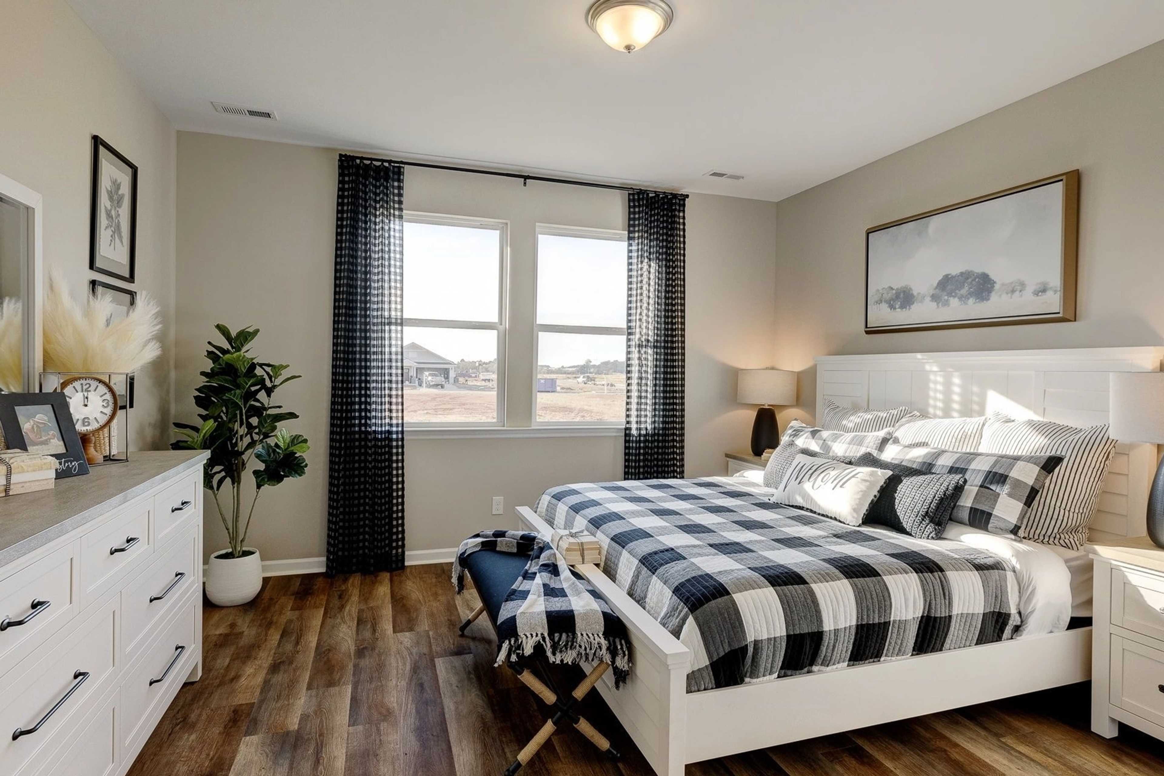 Spacious primary bedroom in Carroll Green, Harvest Alabama with checkered bedding, hardwood floors, and large windows